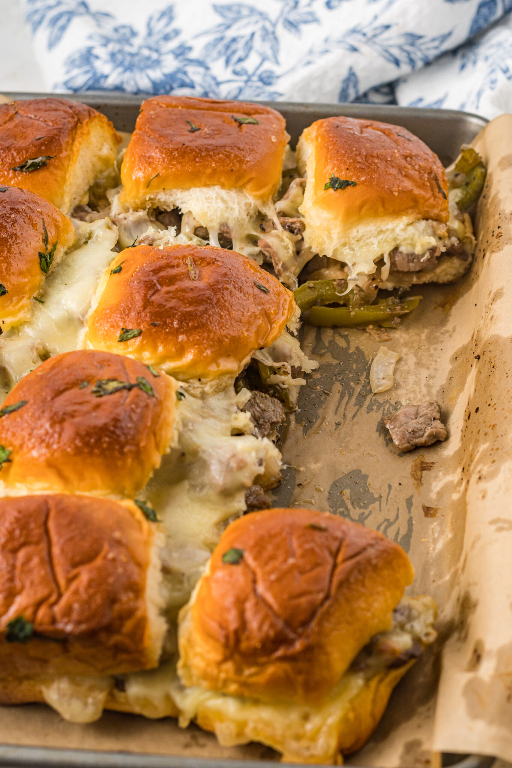 Philly Cheesesteak Sliders on a baking sheet with two removed. 