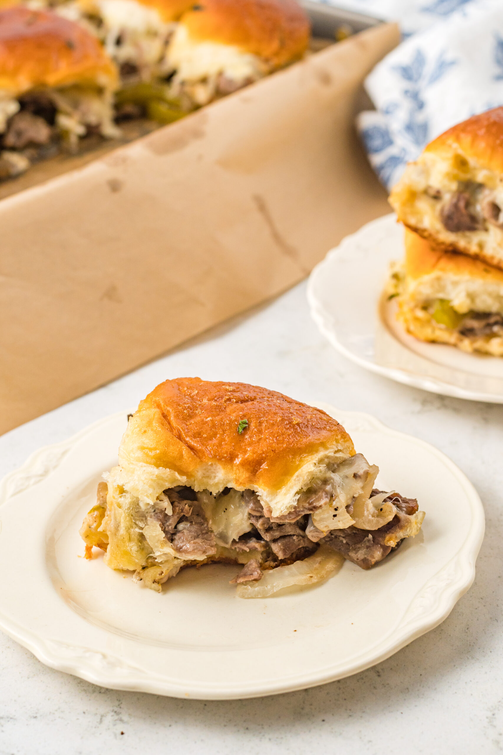 One slider on a white plate with a bite removed showing the cheesy inside. 