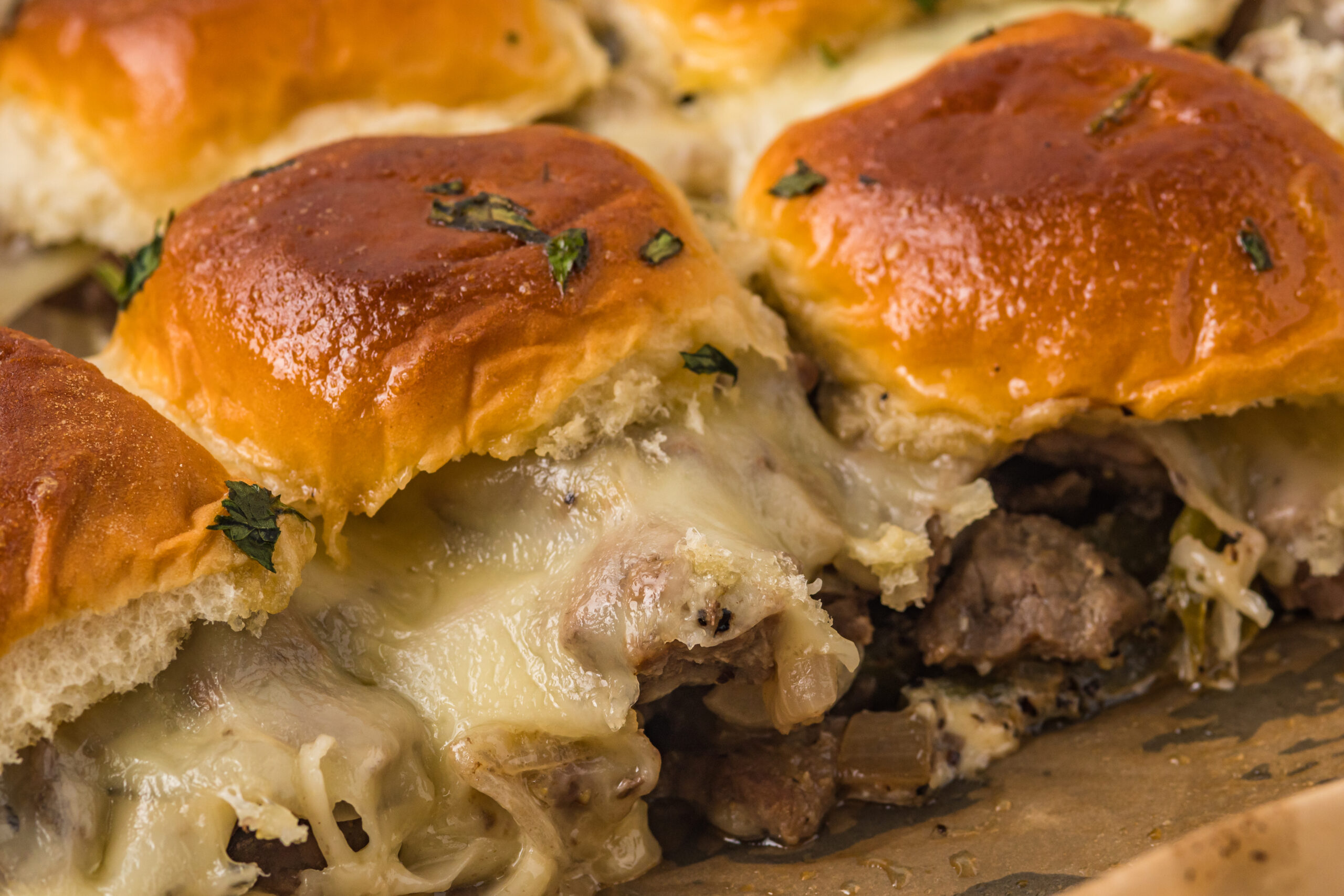 Philly Cheesesteak Sliders on a baking sheet up close to see melty cheese and texture.