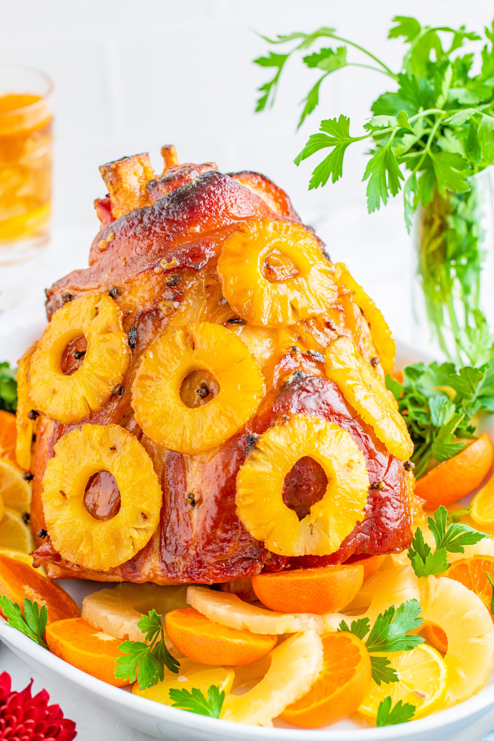 Pineapple Baked Ham covered in pineapple on a large white dish with oranges and pineapple slices lining the bottom.