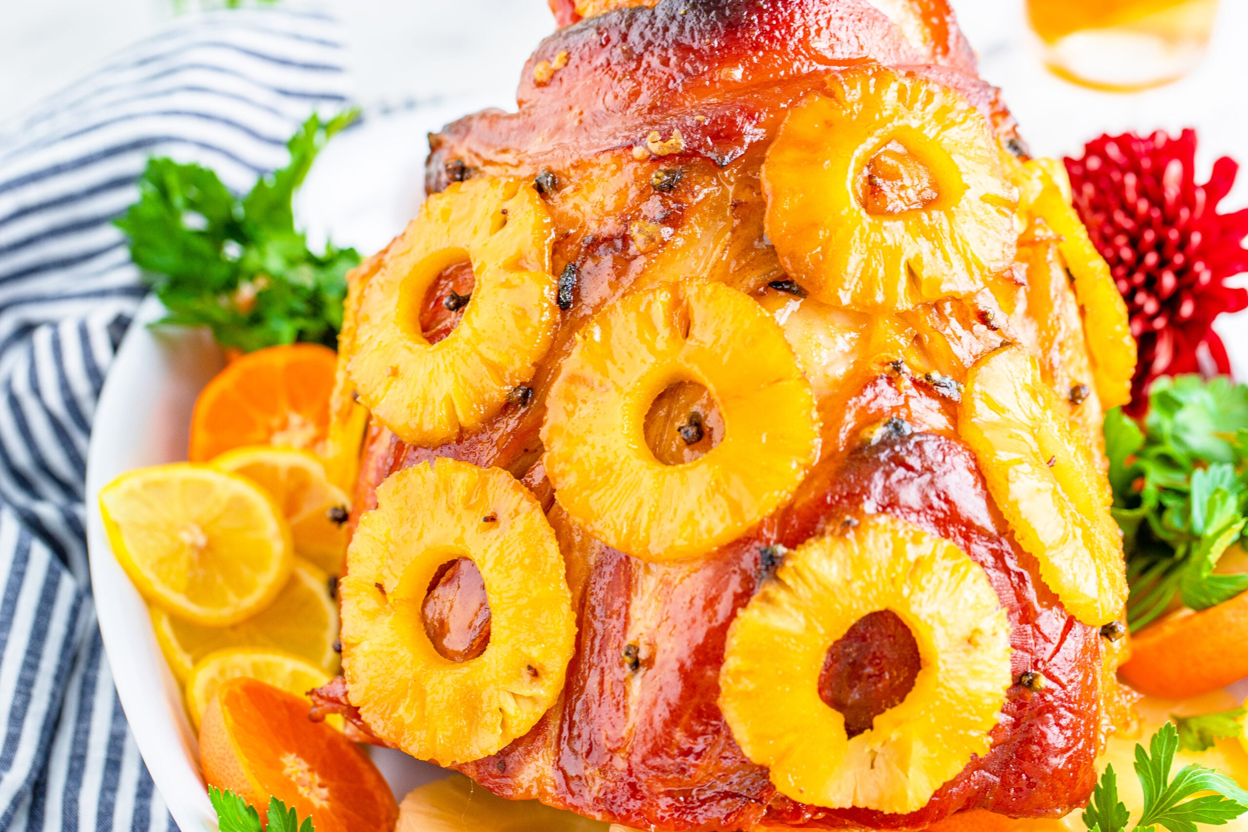 Pineapple Baked Ham covered in pineapple on a large white dish with oranges and pineapple slices lining the bottom.