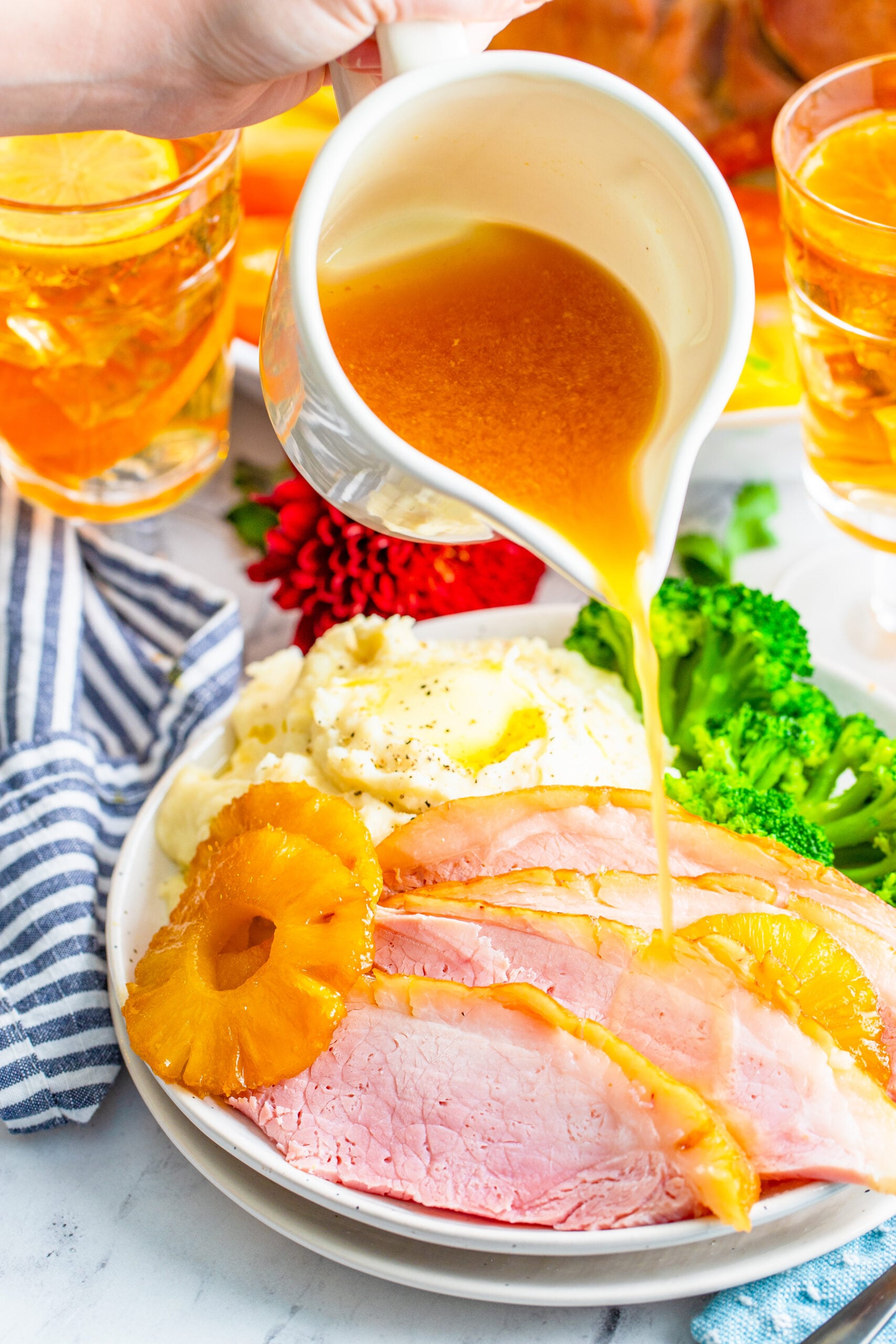 pouring gravy over top the sliced and plated pineapple baked ham.
