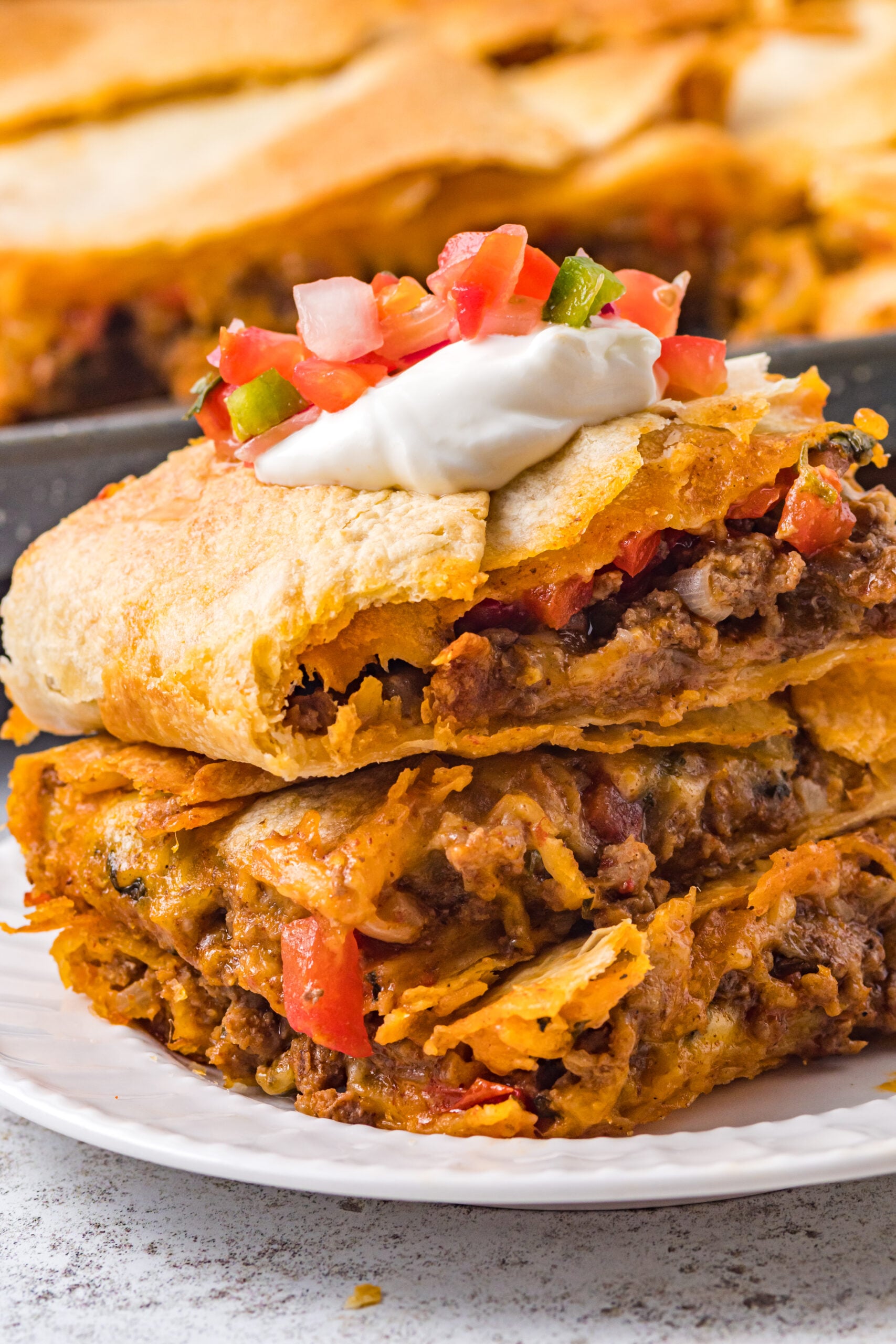 Three slices of sheet pan tacos stacked on a white plate and topped with Pico de Gallo. 