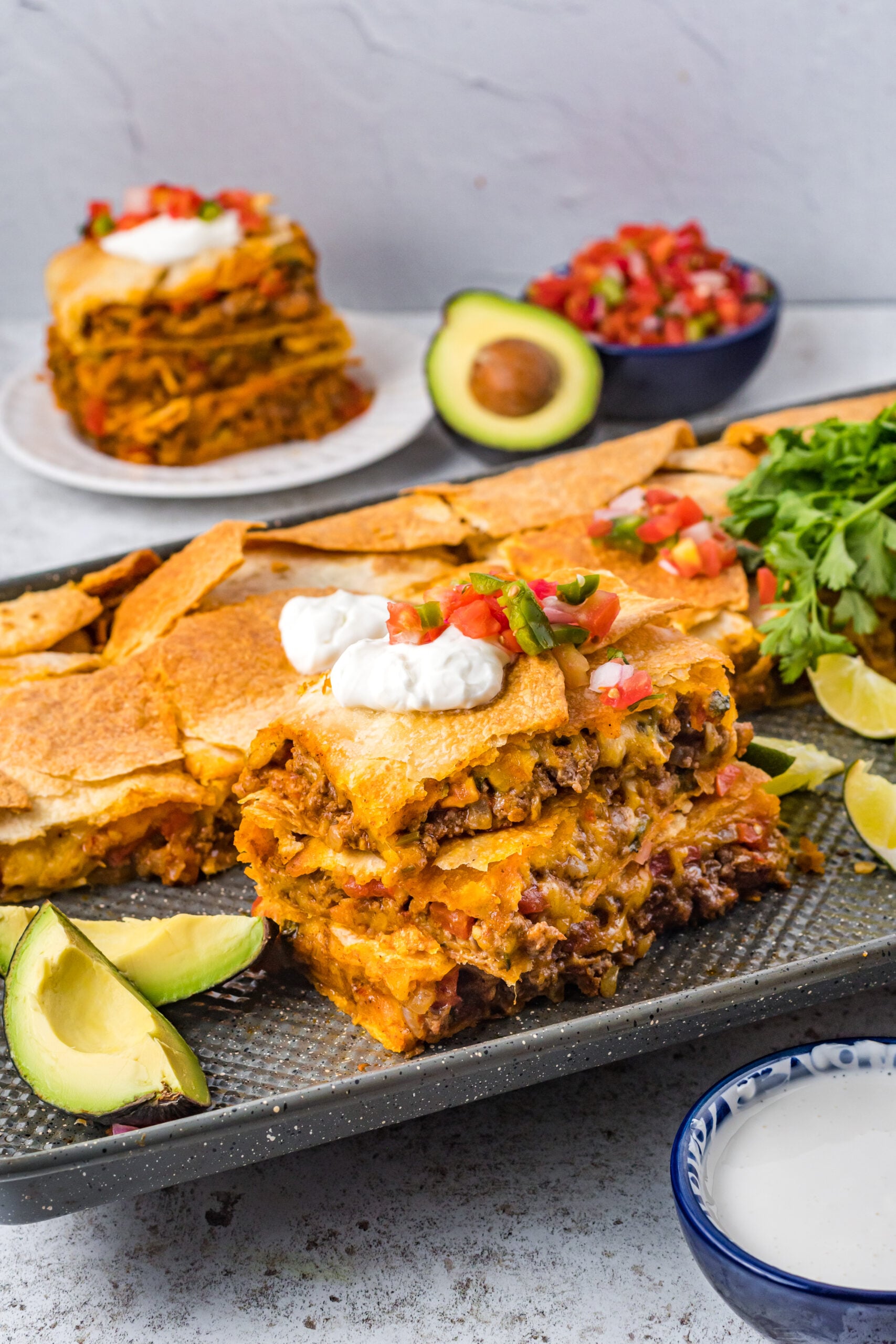 Three slices of sheet pan tacos stacked on the baking sheet topped with sour cream and Pico de Gallo