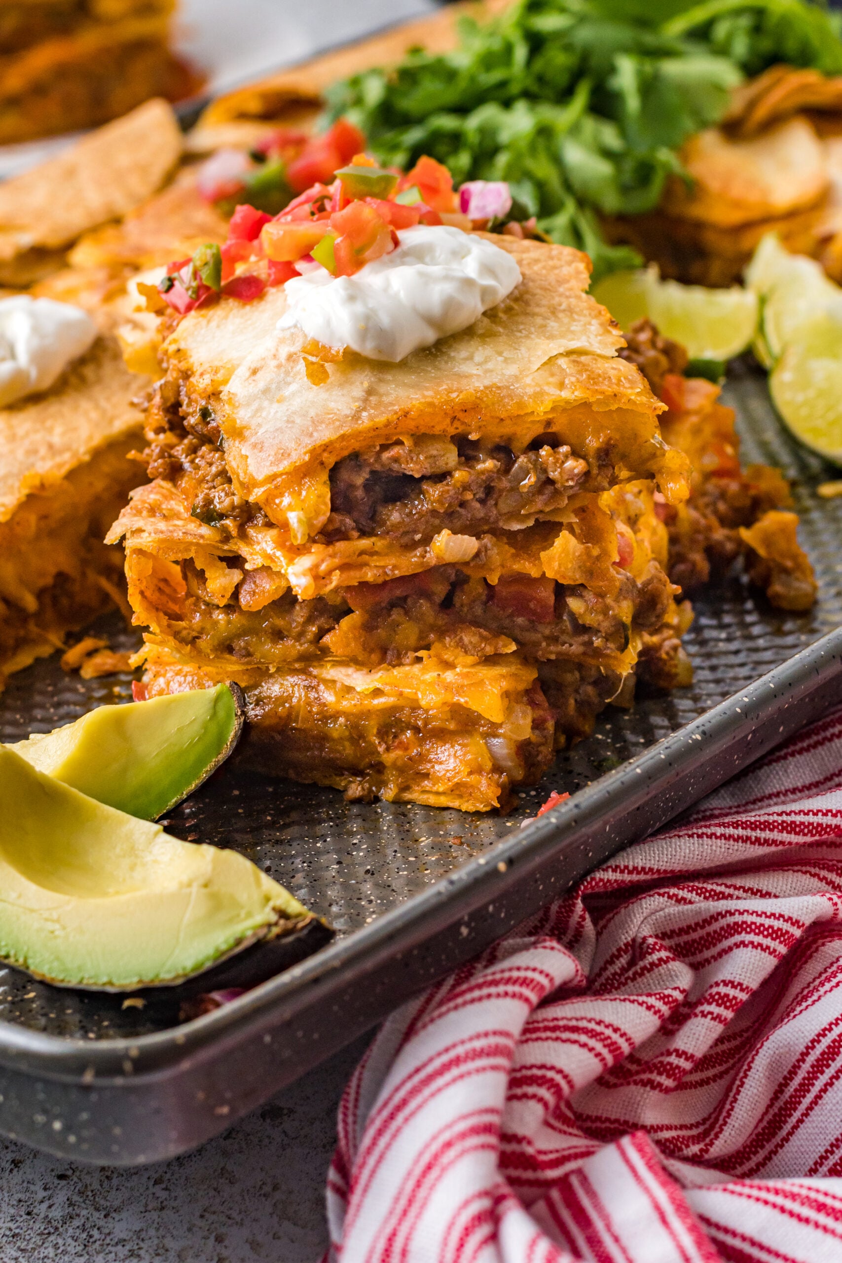 Three slices of sheet pan tacos stacked on the baking sheet topped with sour cream and Pico de Gallo