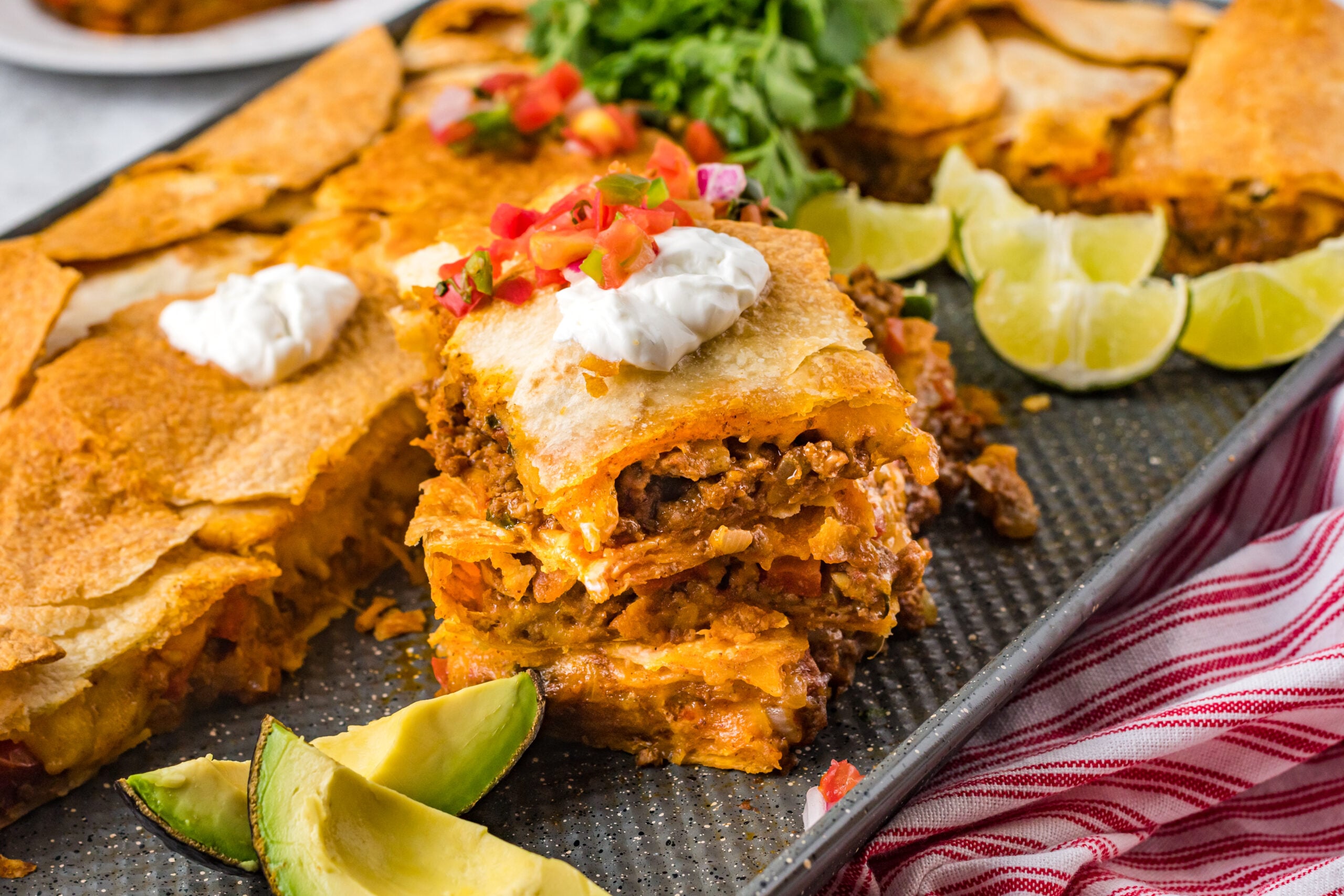 Three slices of sheet pan tacos stacked on the baking sheet topped with sour cream and Pico de Gallo