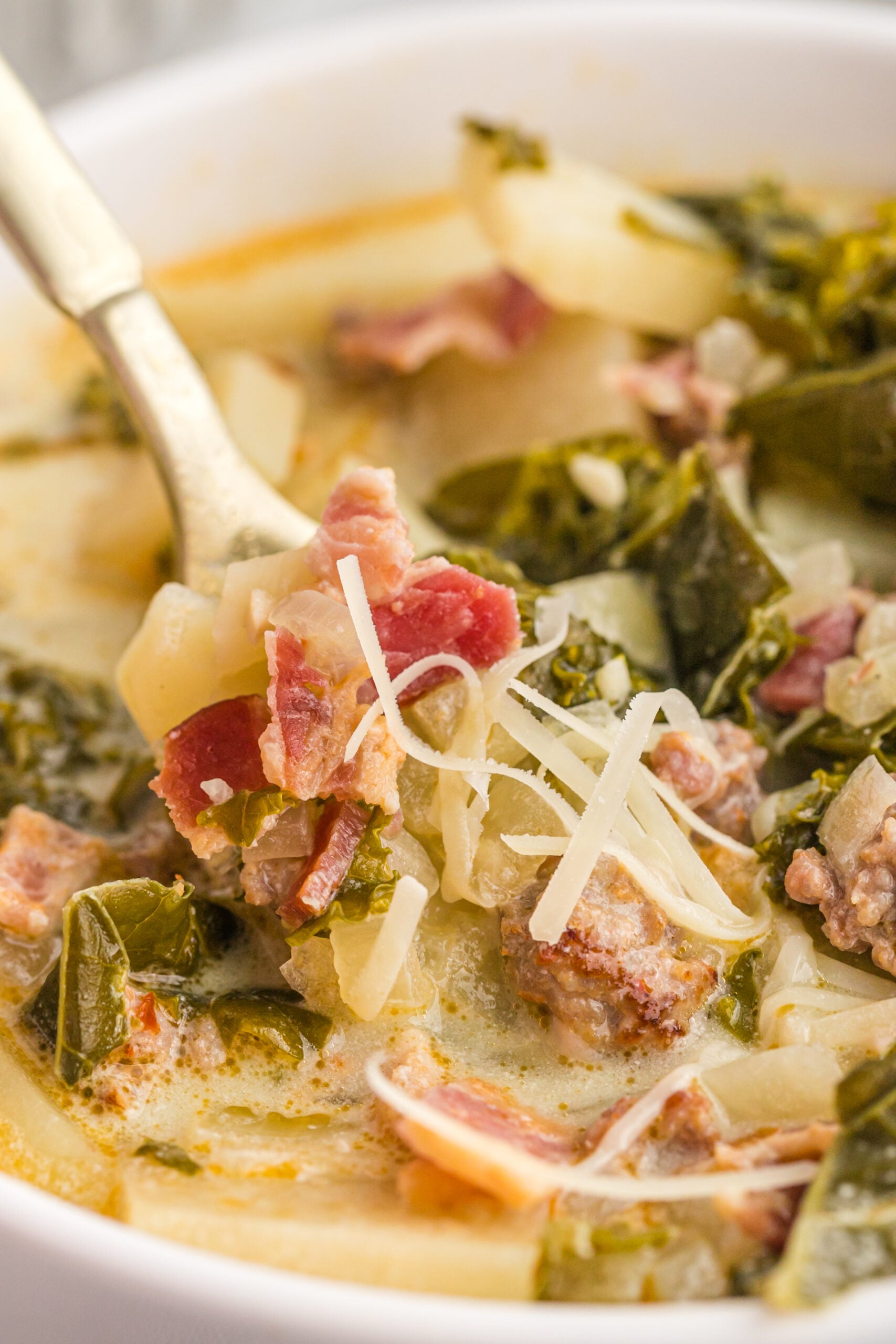 A gold spoon removing Zuppa Toscana Soup from the bowl. 