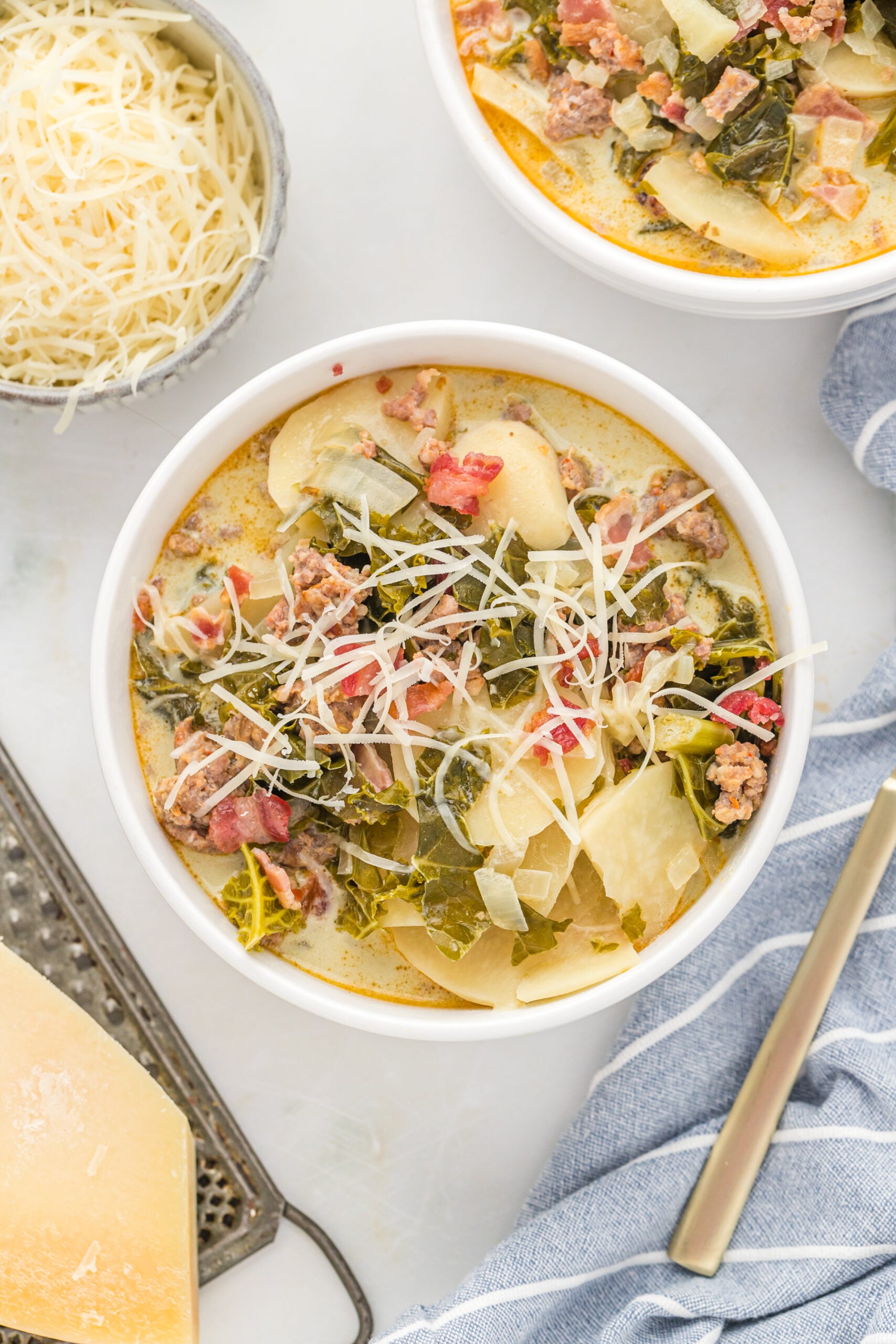 Overhead view of the soup in white bowls topped with shredded cheese with a blue and white stripped linen in the background. 