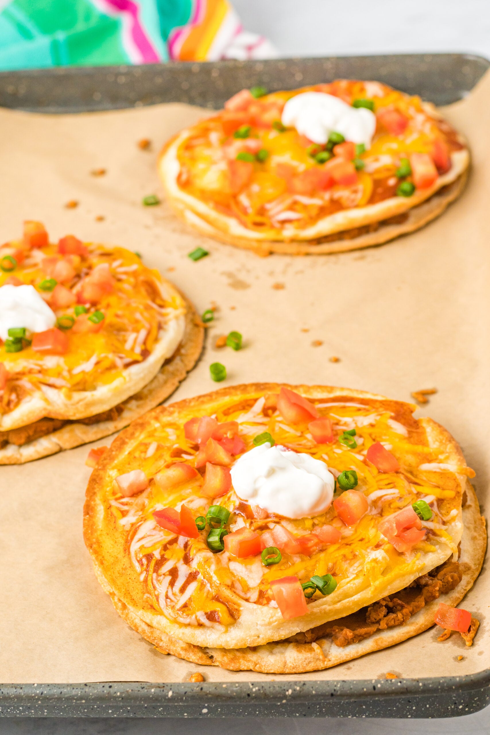 Mexican Pizzas on a baking sheet topped with sour cream, tomatoes, and green onion.