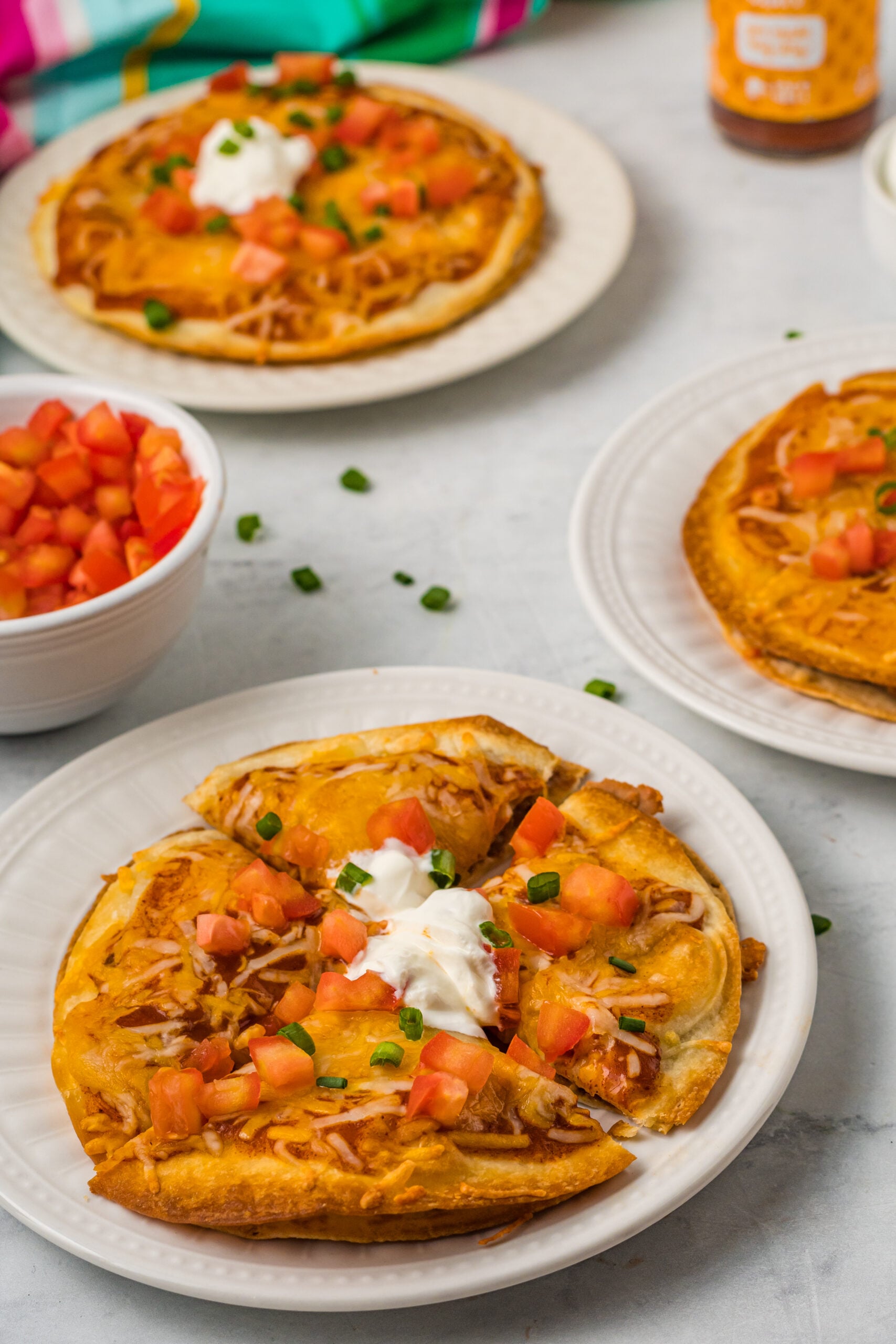 Mexican Pizza on a white plate cut into quarters topped with sour cream, tomatoes, and green onion.