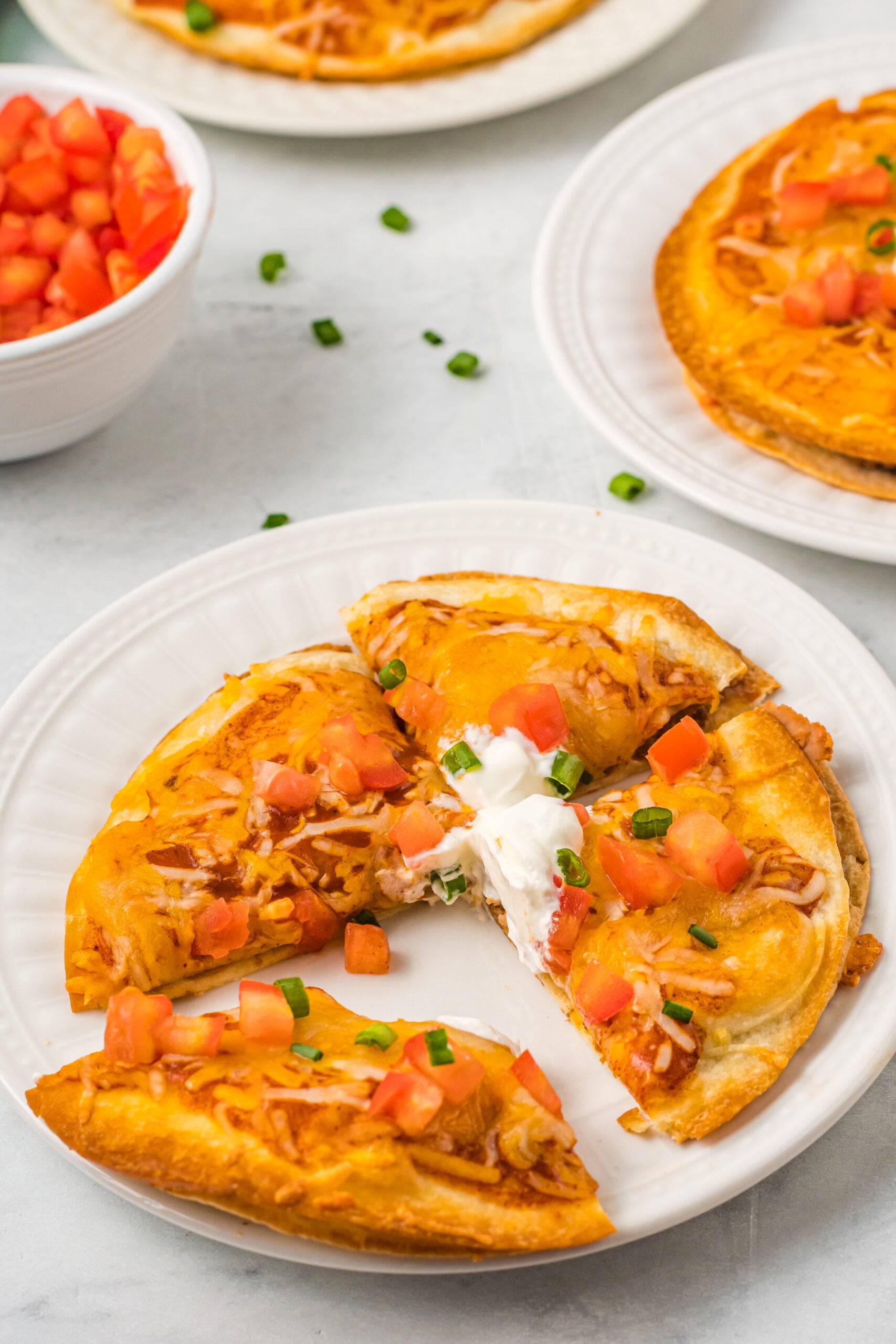Mexican Pizza on a white plate cut into quarters topped with sour cream, tomatoes, and green onion.