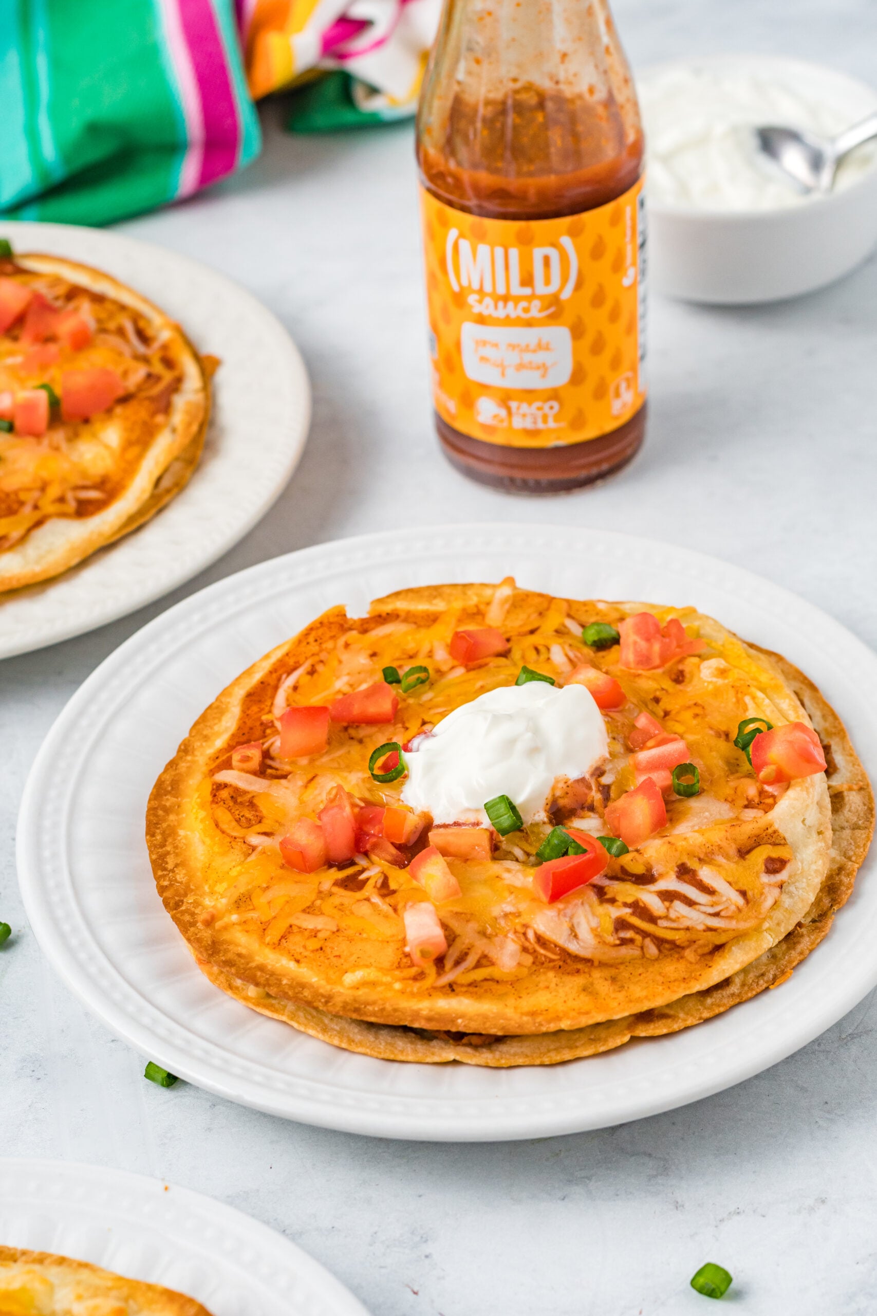 Mexican Pizza on a white plate topped with sour cream, tomatoes, and green onion.