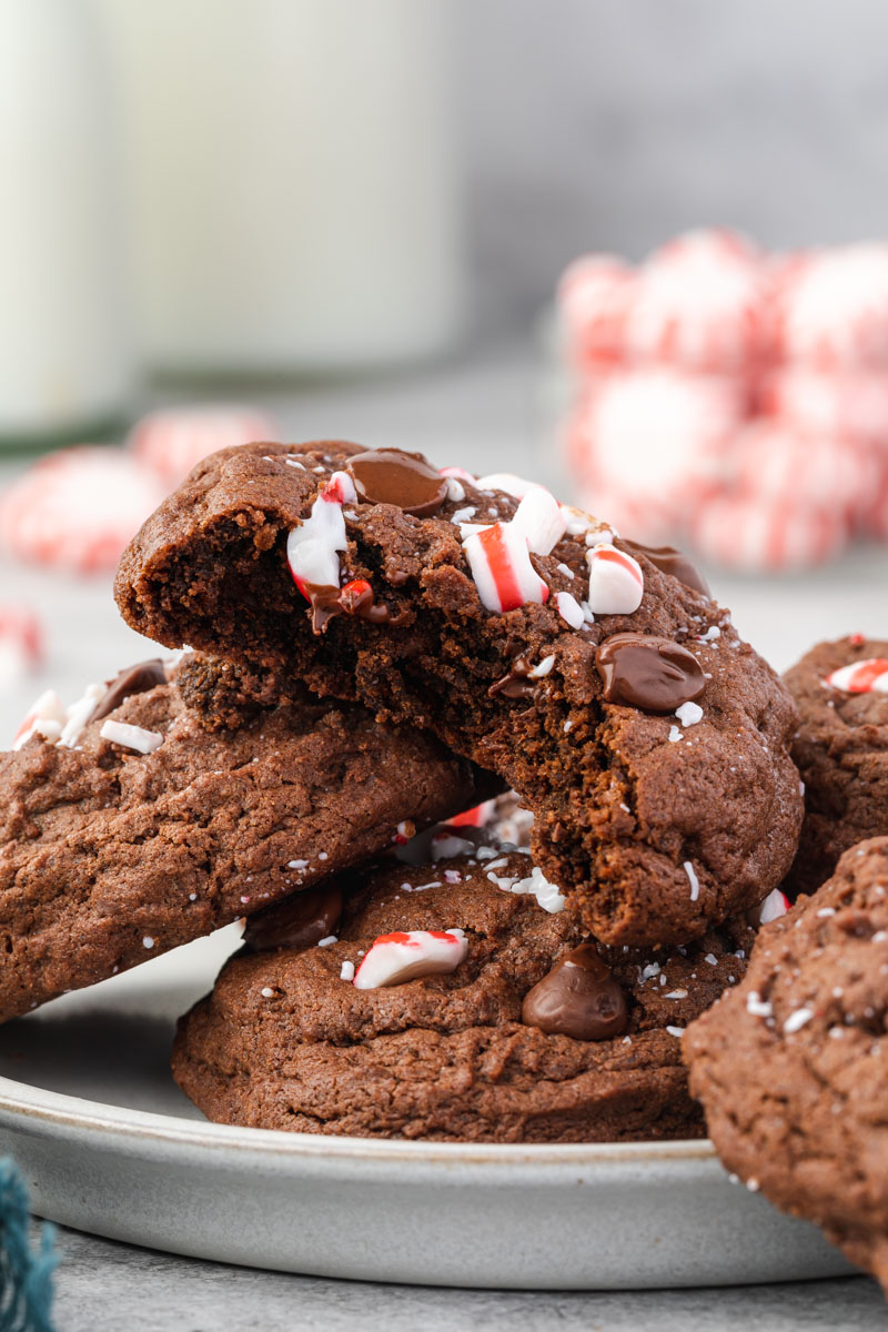 Three Chocolate Peppermint cookies stacked on a white plate with a bite removed from the top cookie showing the inside. 