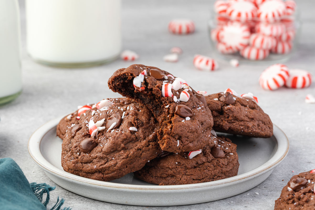 Chocolate Peppermint cookies stacked on a white plate with a bite removed from the top cookie showing the inside. 