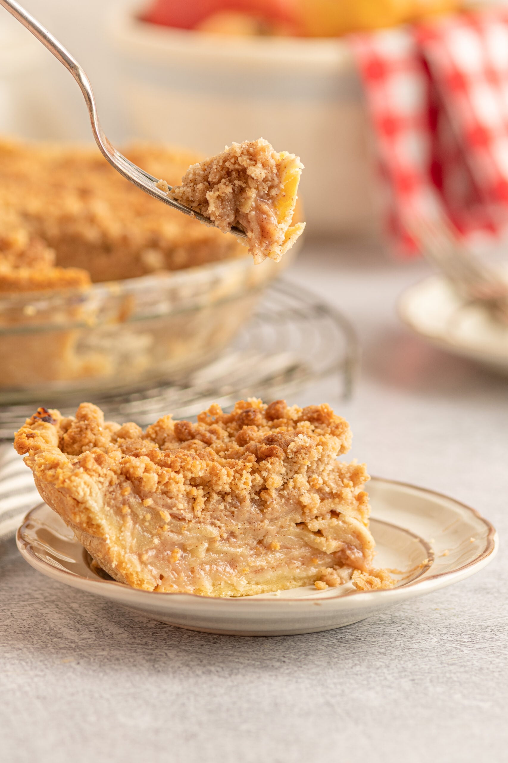 A piece of Dutch apple pie on a tan plate with a piece being removed with a silver fork. 