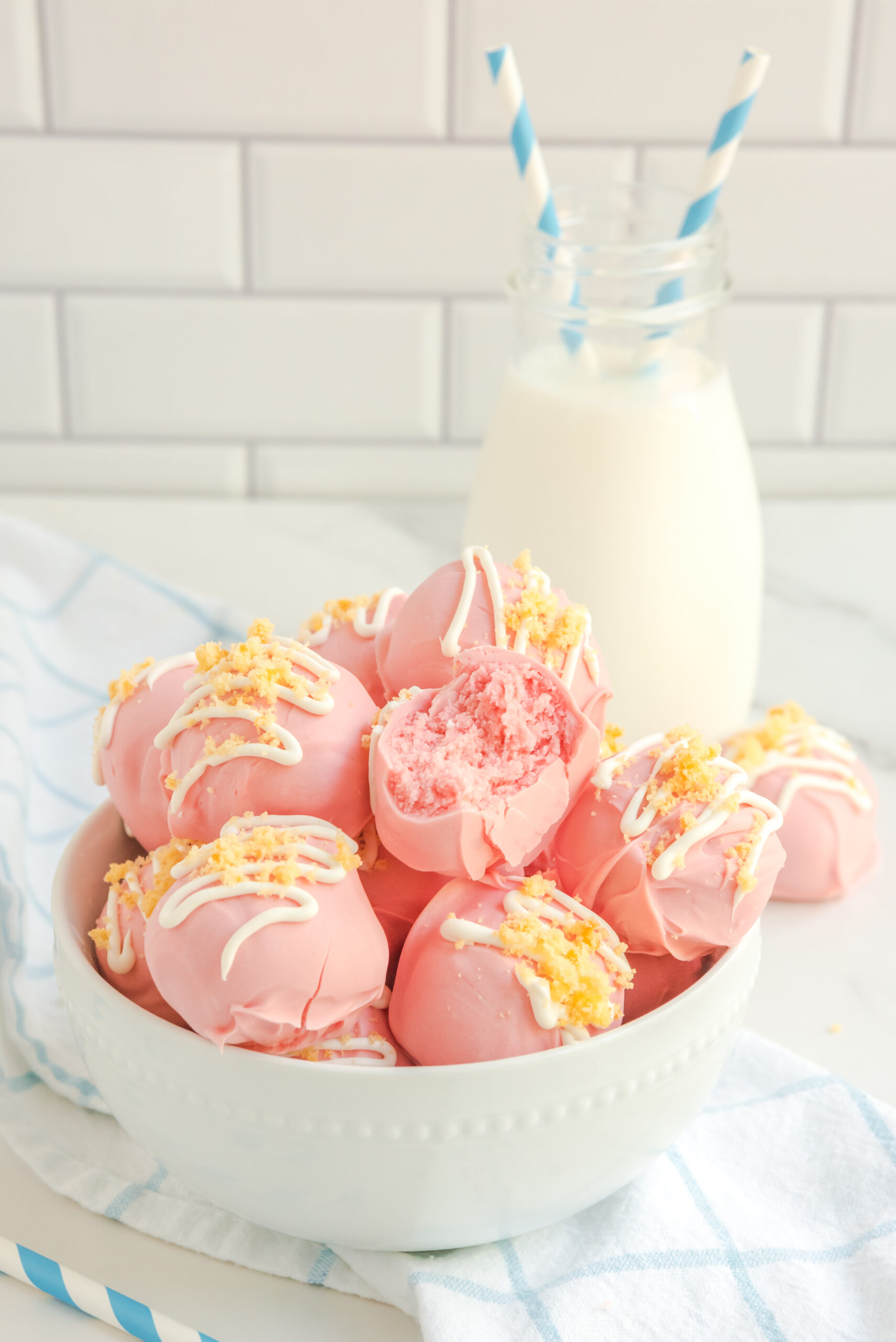 Strawberry truffles stacked on top of each other in a white bowl with milk and blue and white straws in the background. 