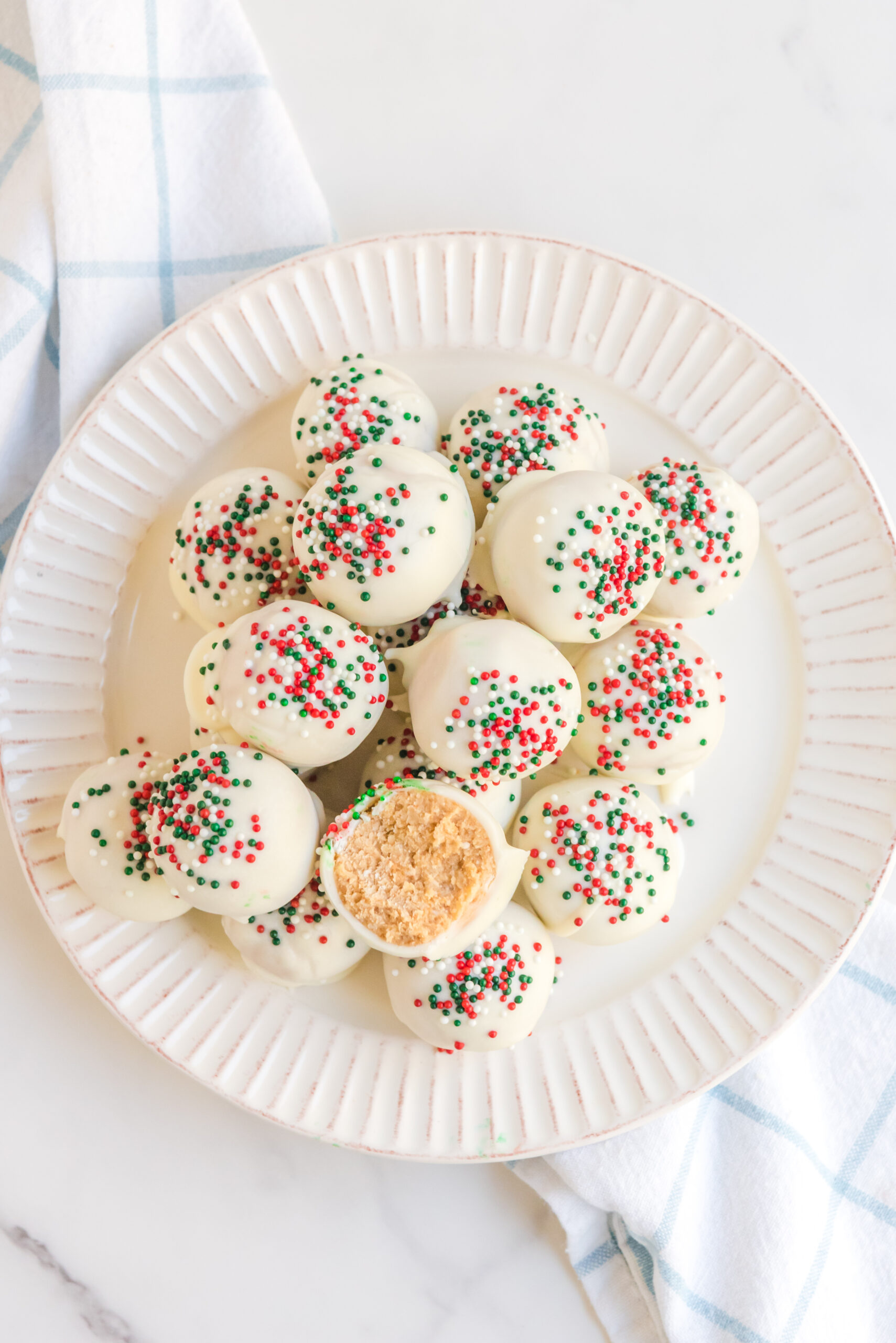 Overhead view of White Chocolate Truffles stacked on a white plate topped with red, white, and green sprinkles. 