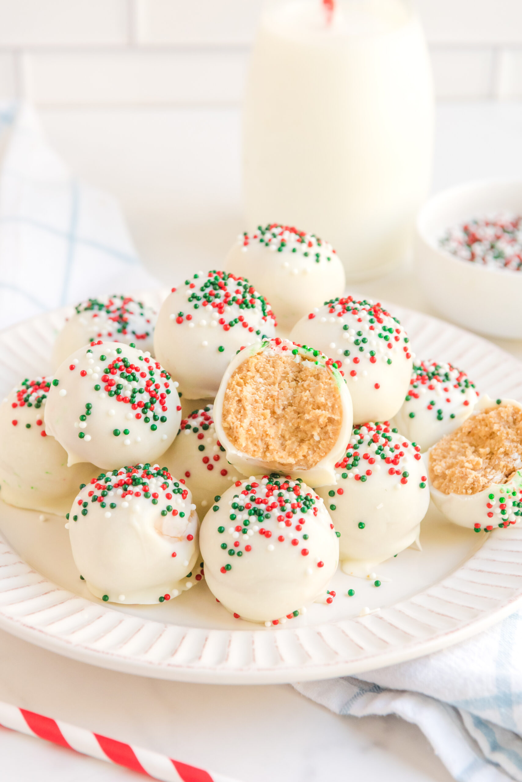 White Chocolate Truffles stacked on a white plate topped with red, white, and green sprinkles. 