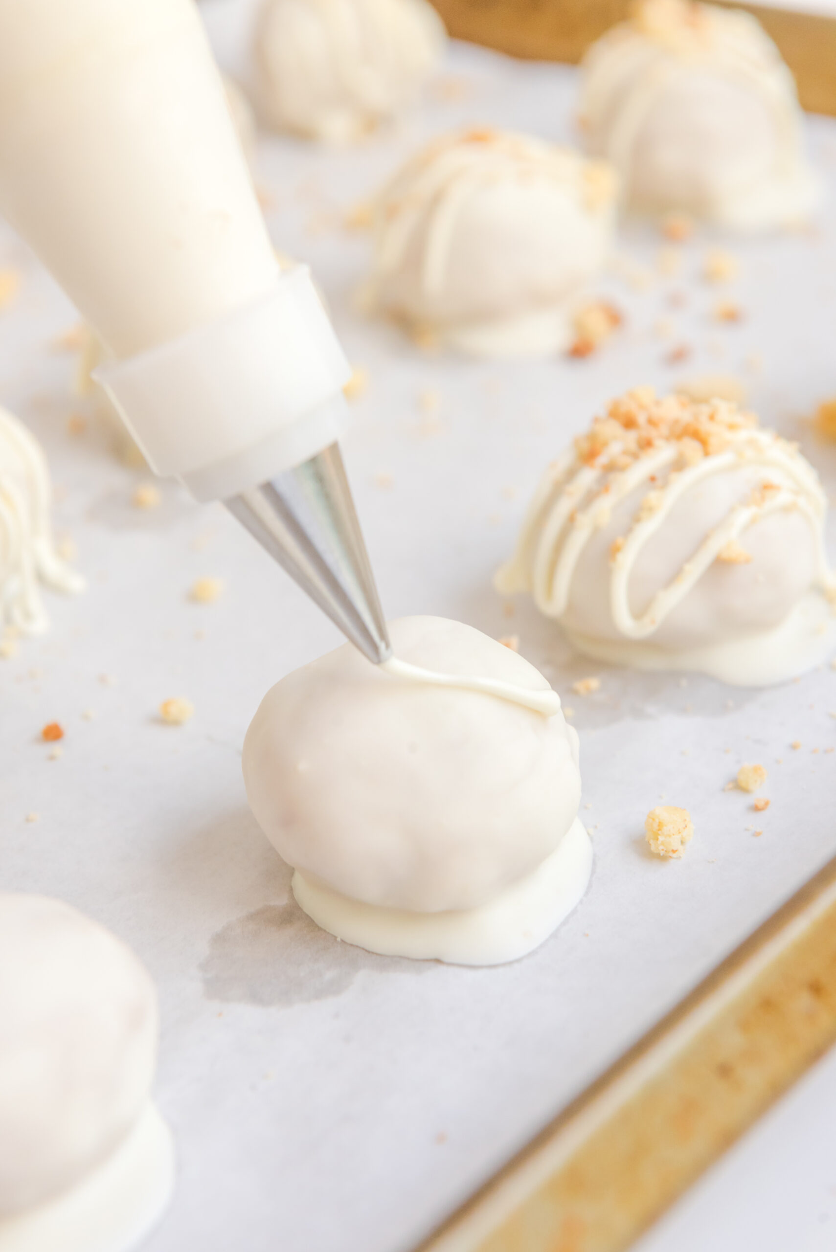 Photo of a piping bag piping on a white chocolate drizzle on top of each truffle. 
