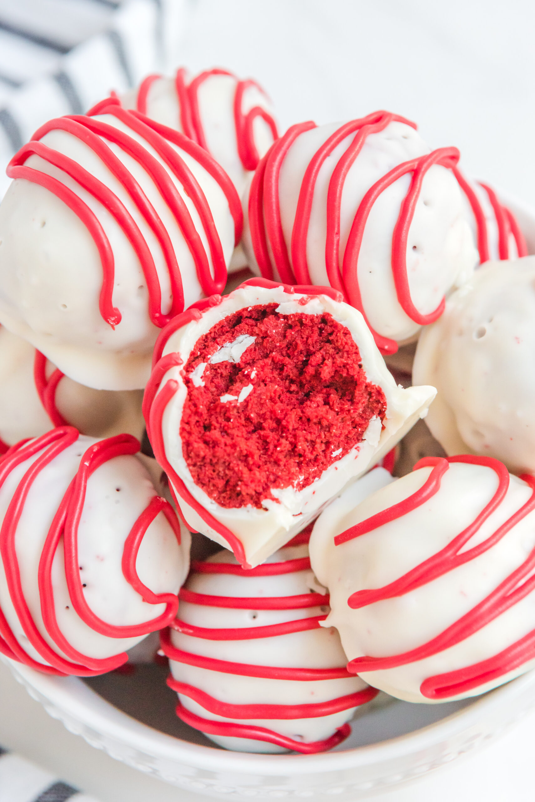 A red velvet cake ball stacked on top of other truffles with a bite removed showing the inside.