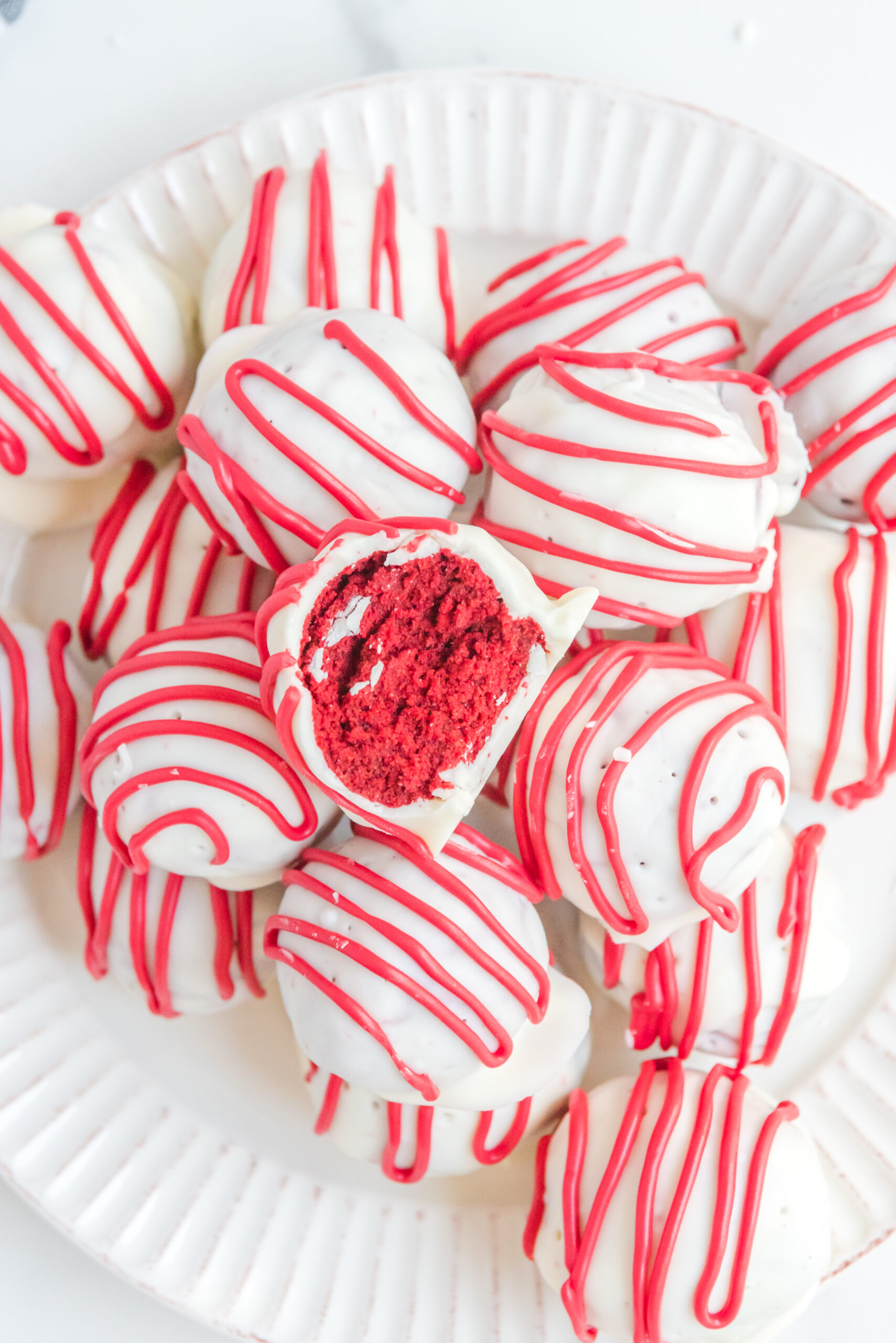 A red velvet cake ball stacked on top of other truffles with a bite removed showing the inside.