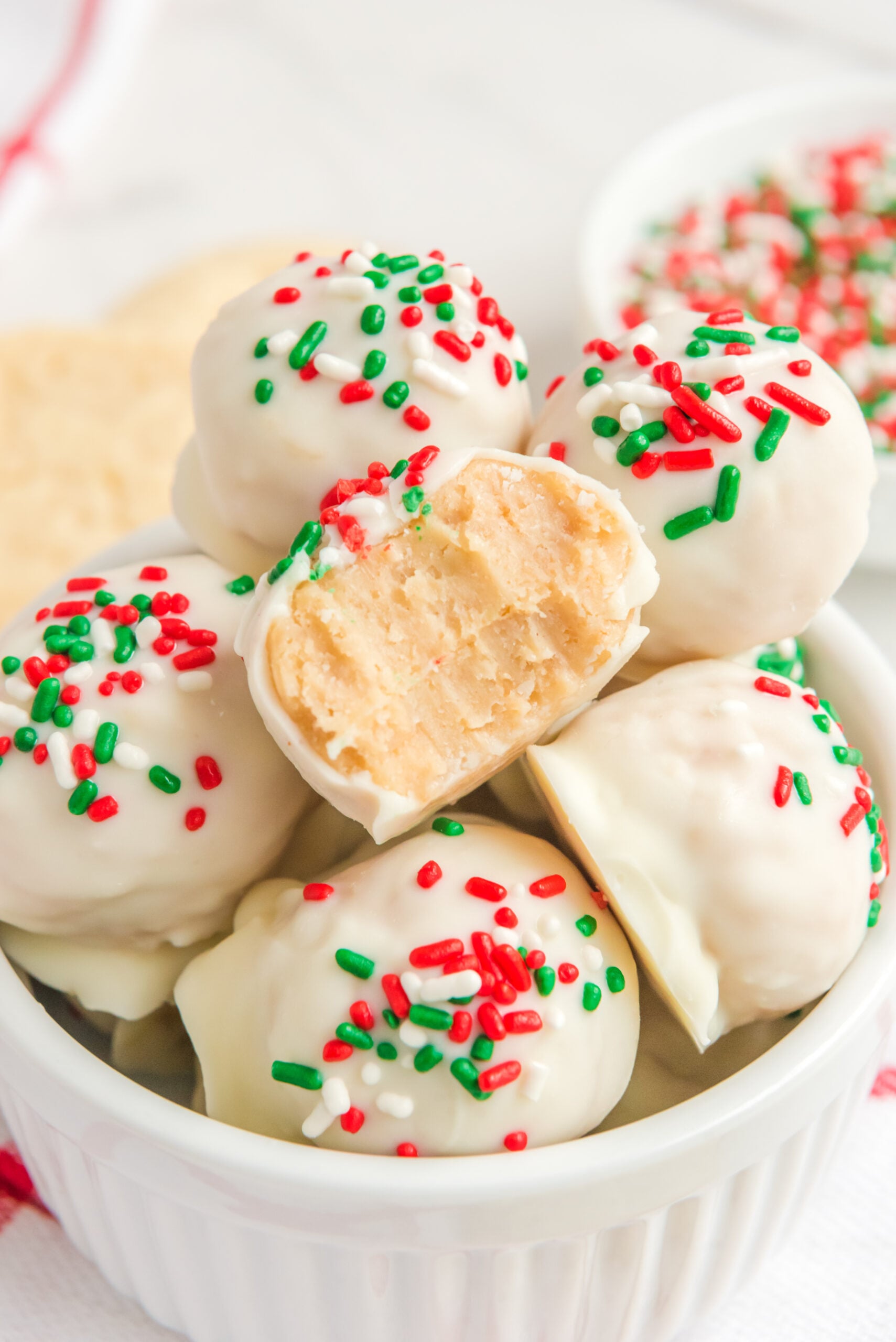 Sugar Cookie Truffles stacked in a small white bowl with a bite removed from one showing the inside.