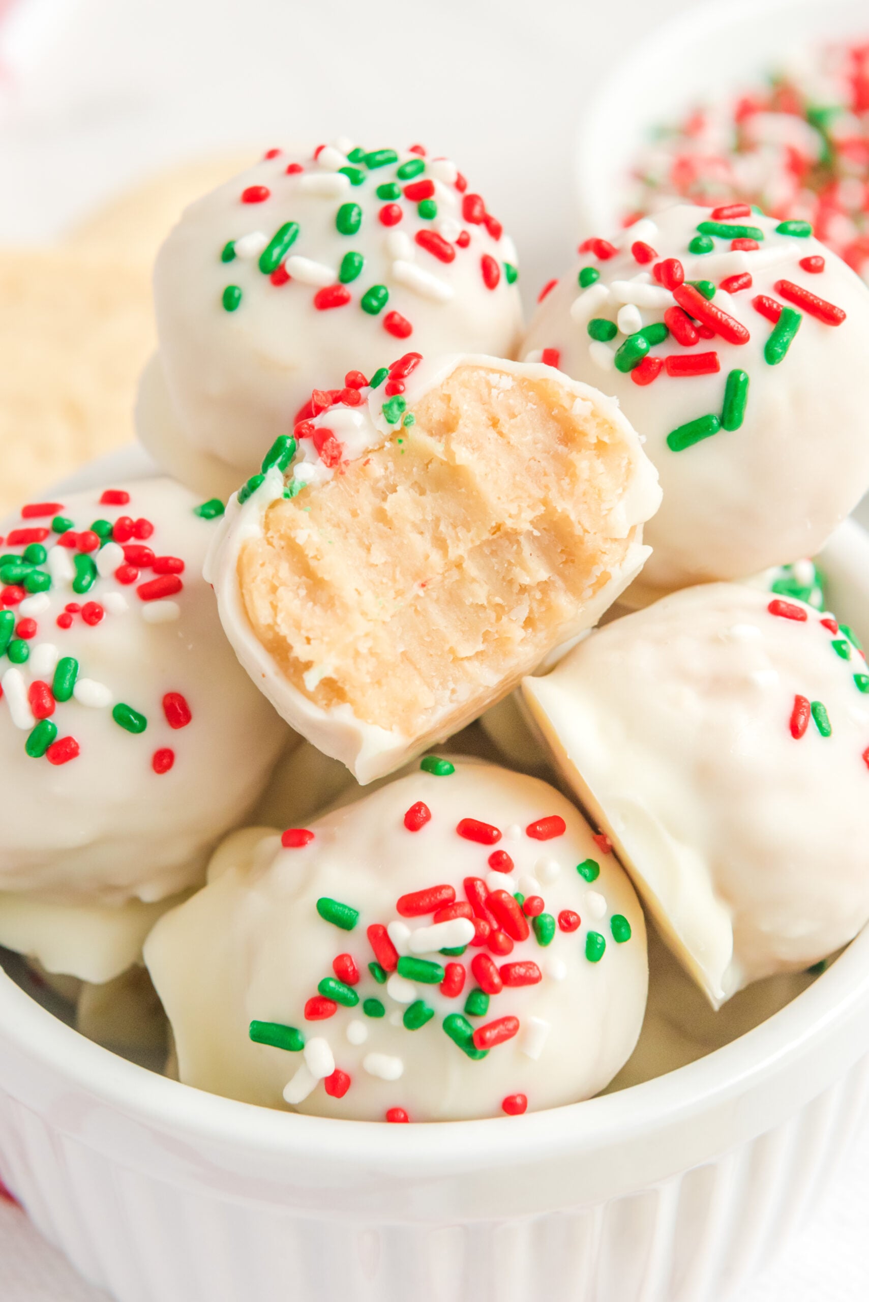 Sugar Cookie Truffles stacked in a small white bowl with a bite removed from one showing the inside.