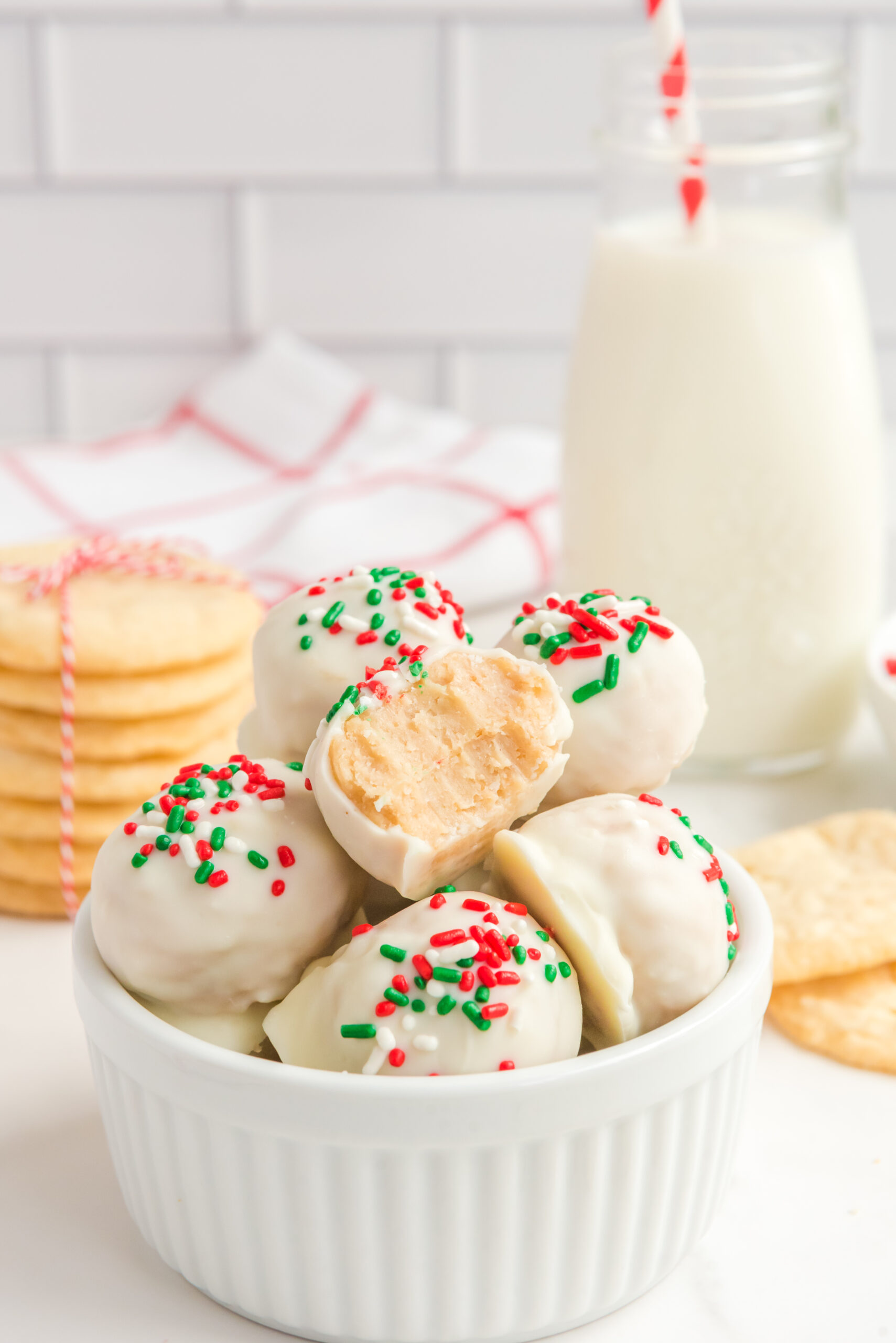Sugar Cookie Truffles stacked in a small white bowl with a bite removed from one showing the inside.