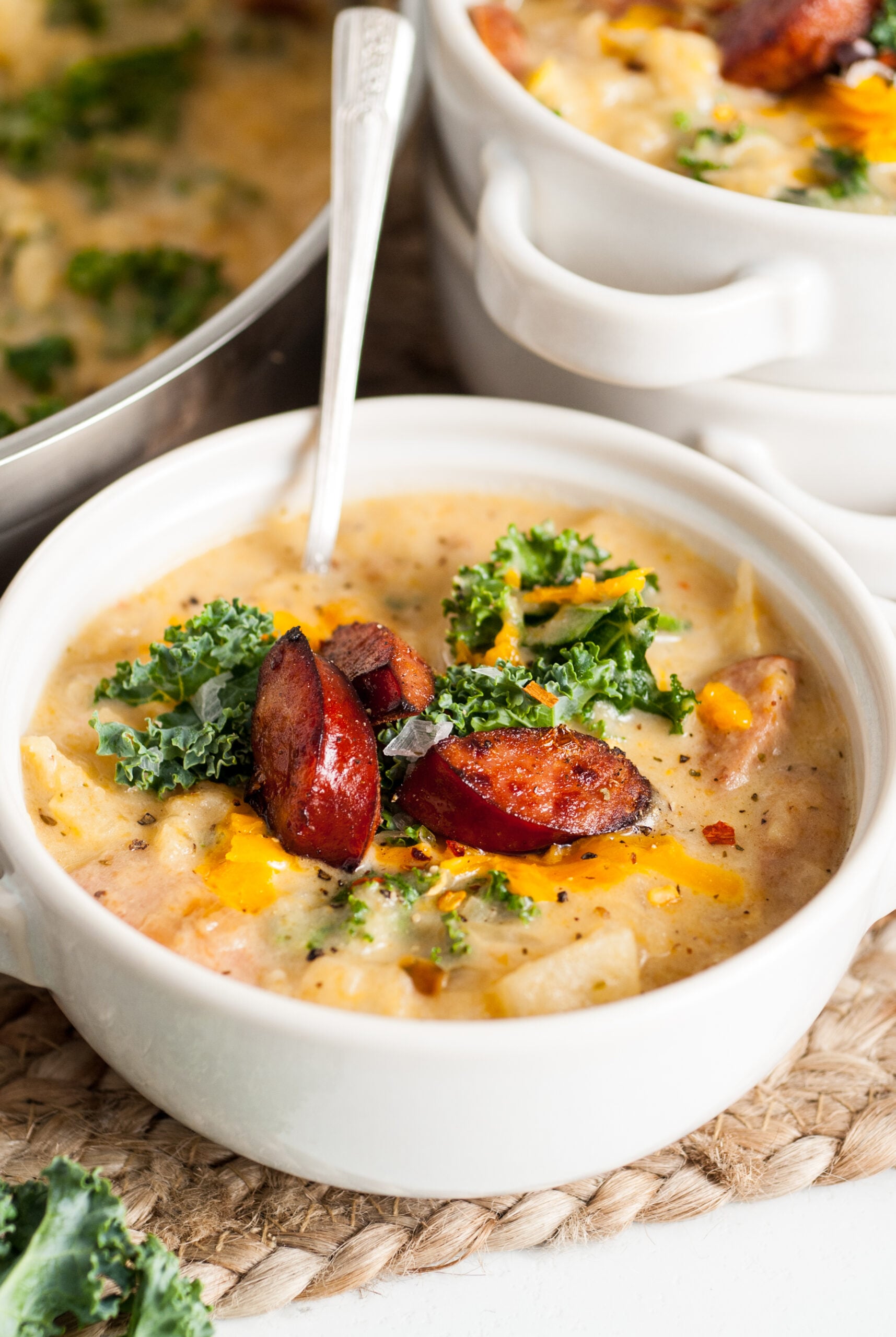 Kielbasa Soup in a white bowl topped with kale and cooked Kielbasa. 