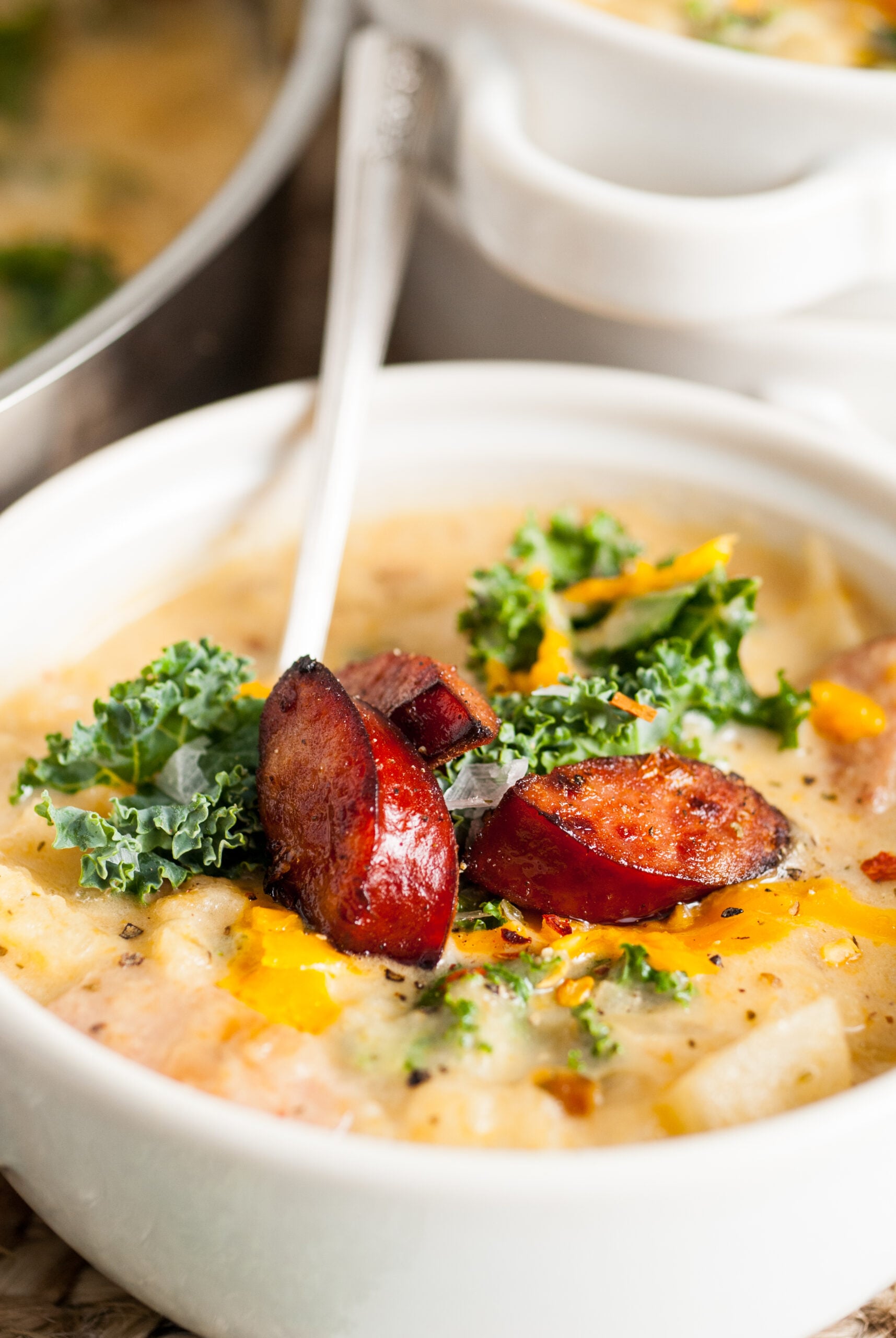 Kielbasa Soup in a white bowl topped with kale and cooked Kielbasa. 
