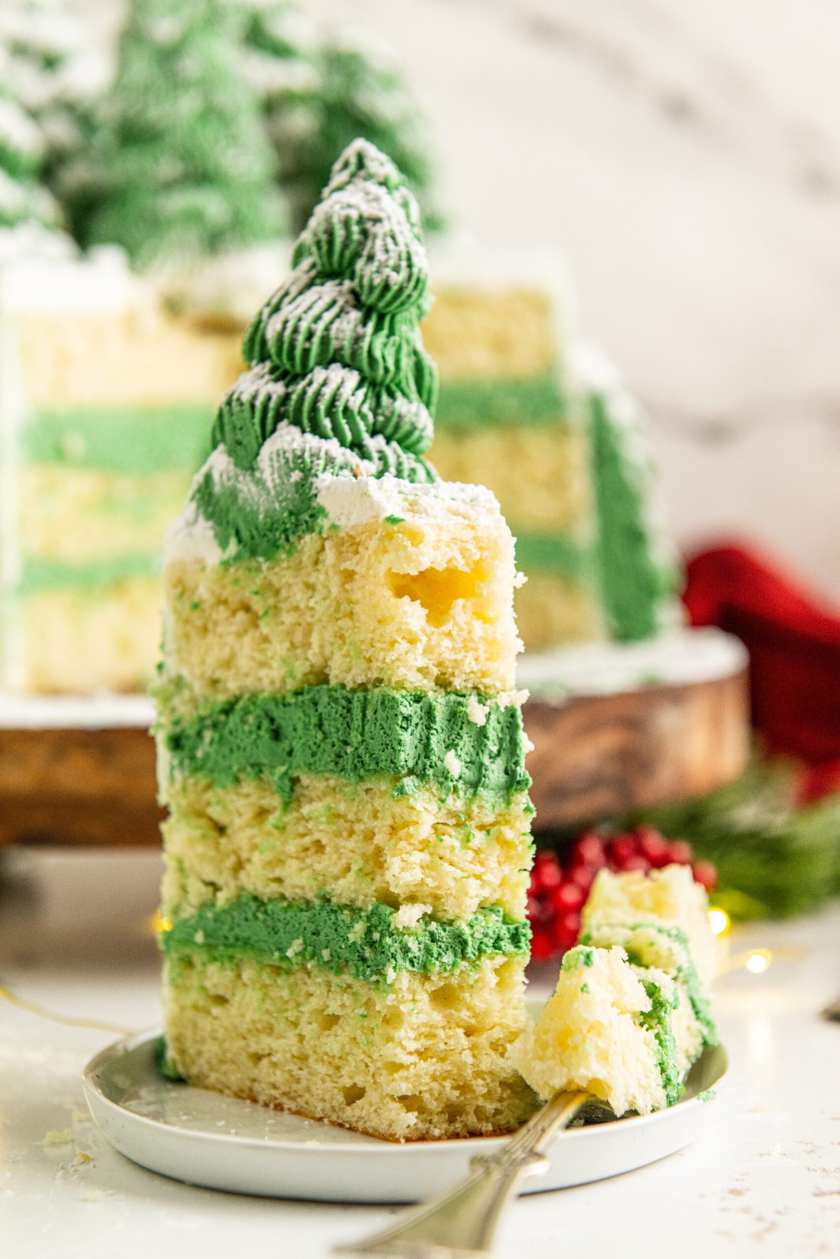 A shot of a piece of Christmas tree cake on a white plate with a bite removed onto a silver fork and placed to the side.