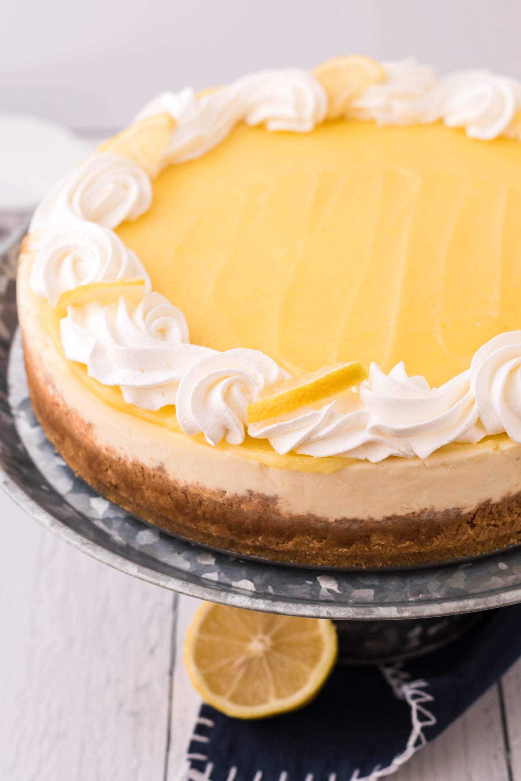 Lemon Curd Cheesecake topped with whipped cream and lemon slices on a metal serving stand.