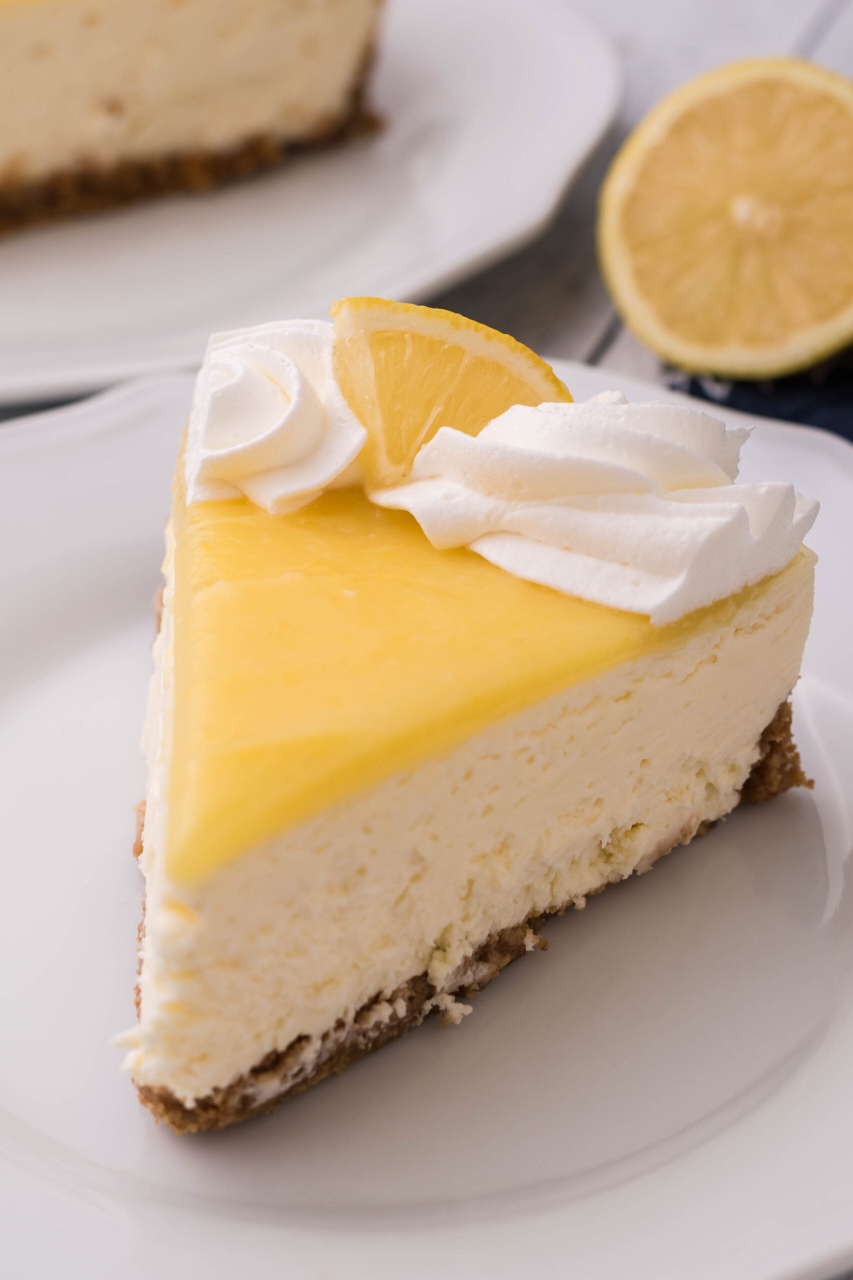 A slice of cheesecake topped with whipped cream and a lemon slice on a white plate.