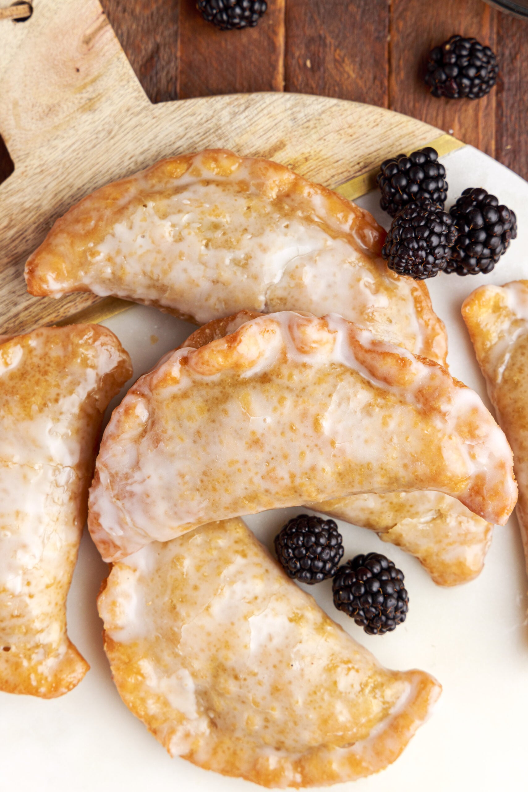 Overhead shot of blackberry hand pies stacked on a marble serving tray with fresh blackberries. 
