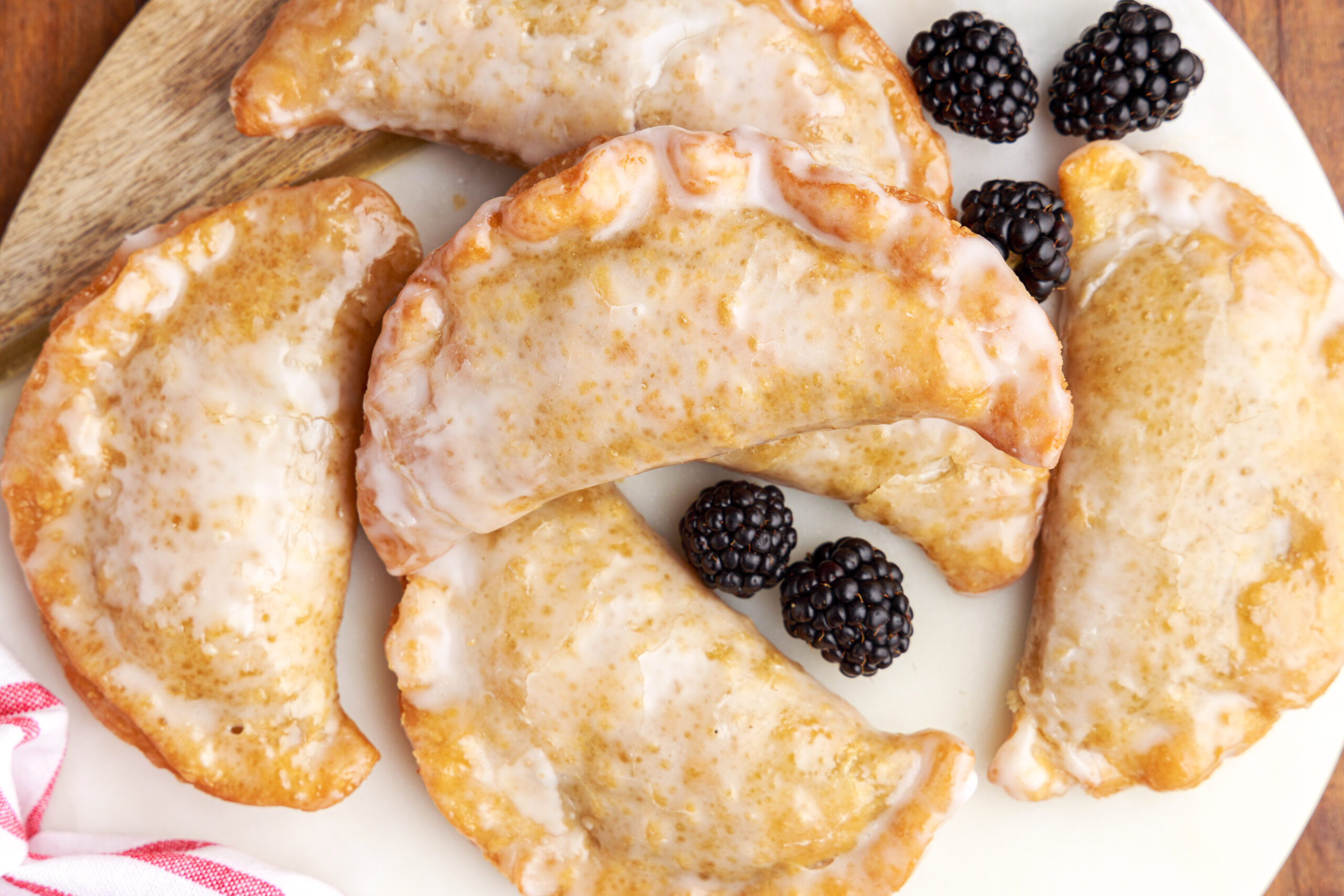 Overhead shot of blackberry hand pies stacked on a marble serving tray with fresh blackberries. 