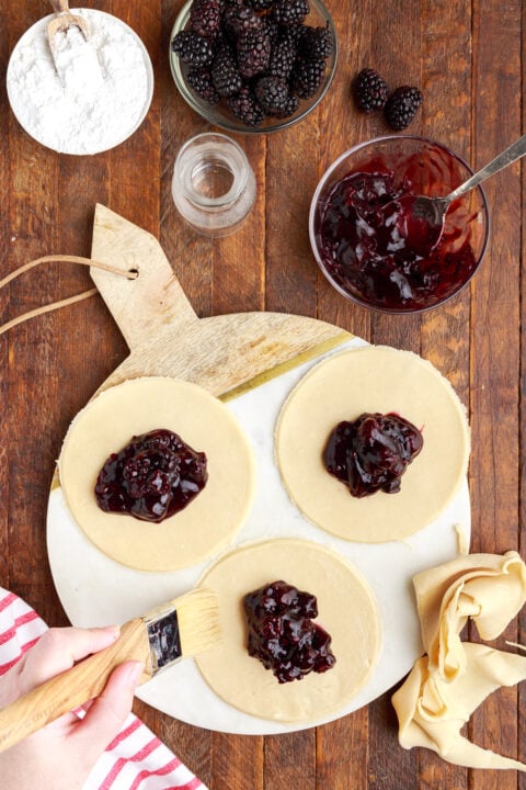 three circle of pie dough on a marble serving tray with blackberry jam in the center of each circle. 