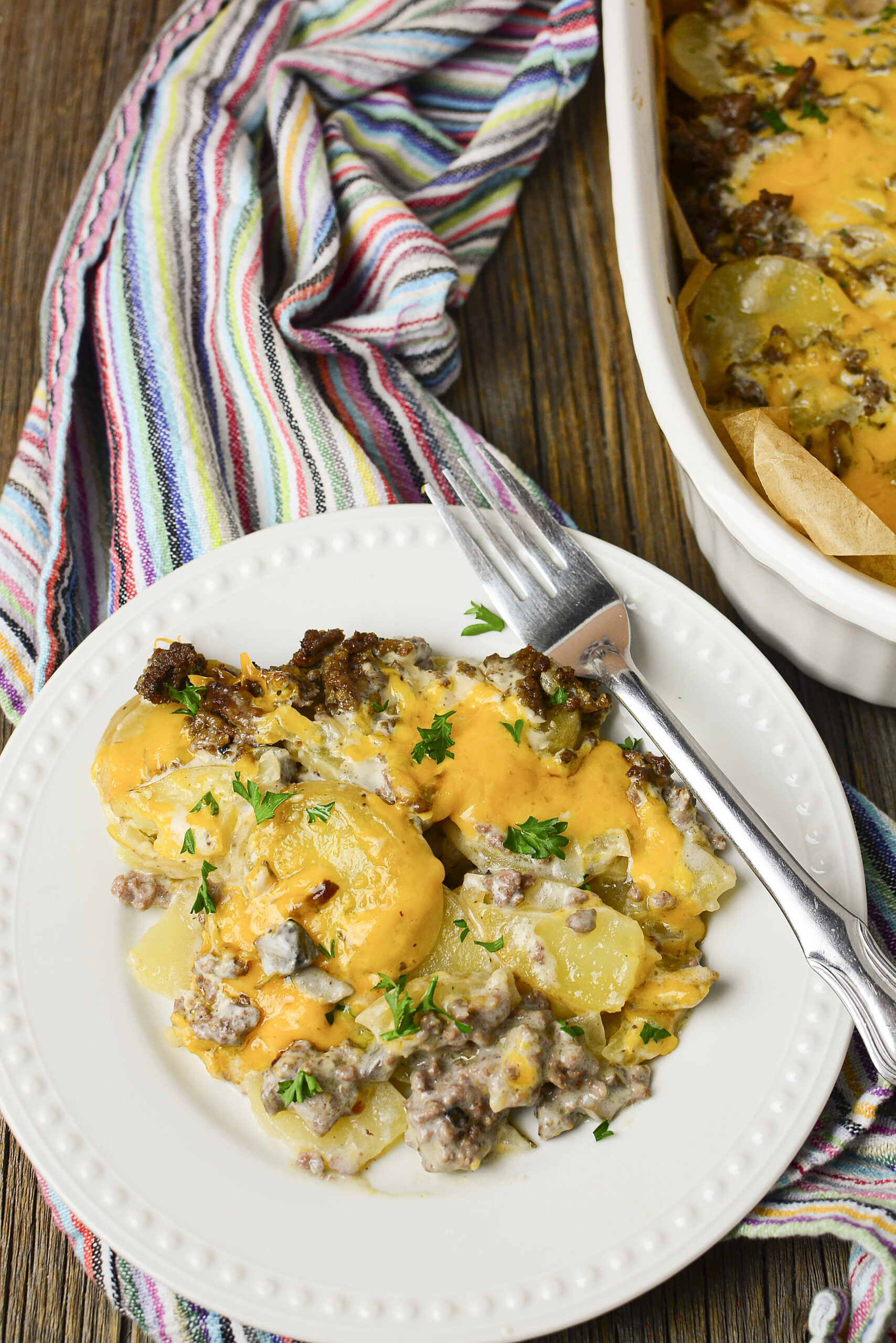 Ground beef and potato casserole on a white plate topped with fresh parsley. 