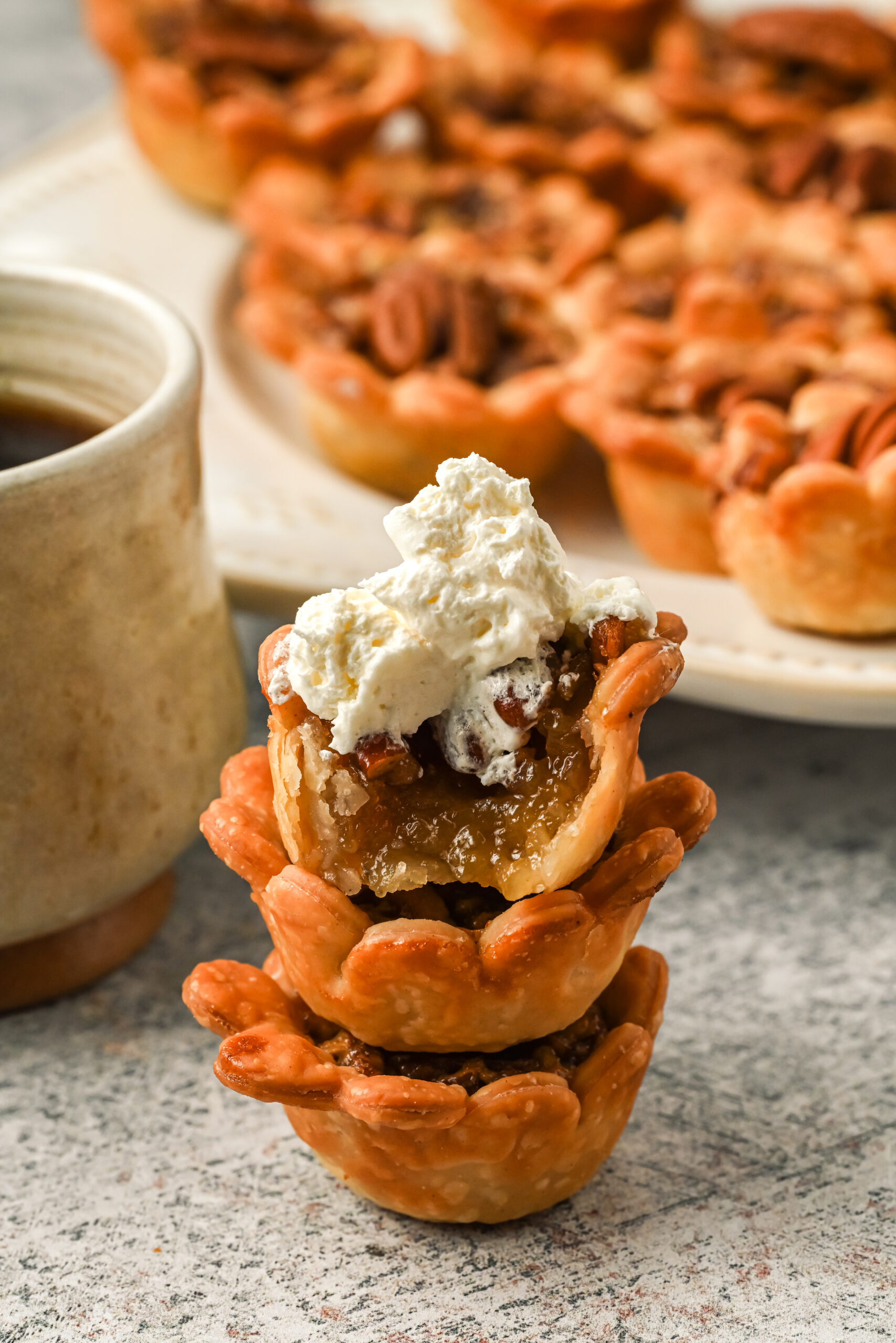 Three mini pies stacked on top of each other with whipped cream on top. A bite is removed from the top pie showing the filling.