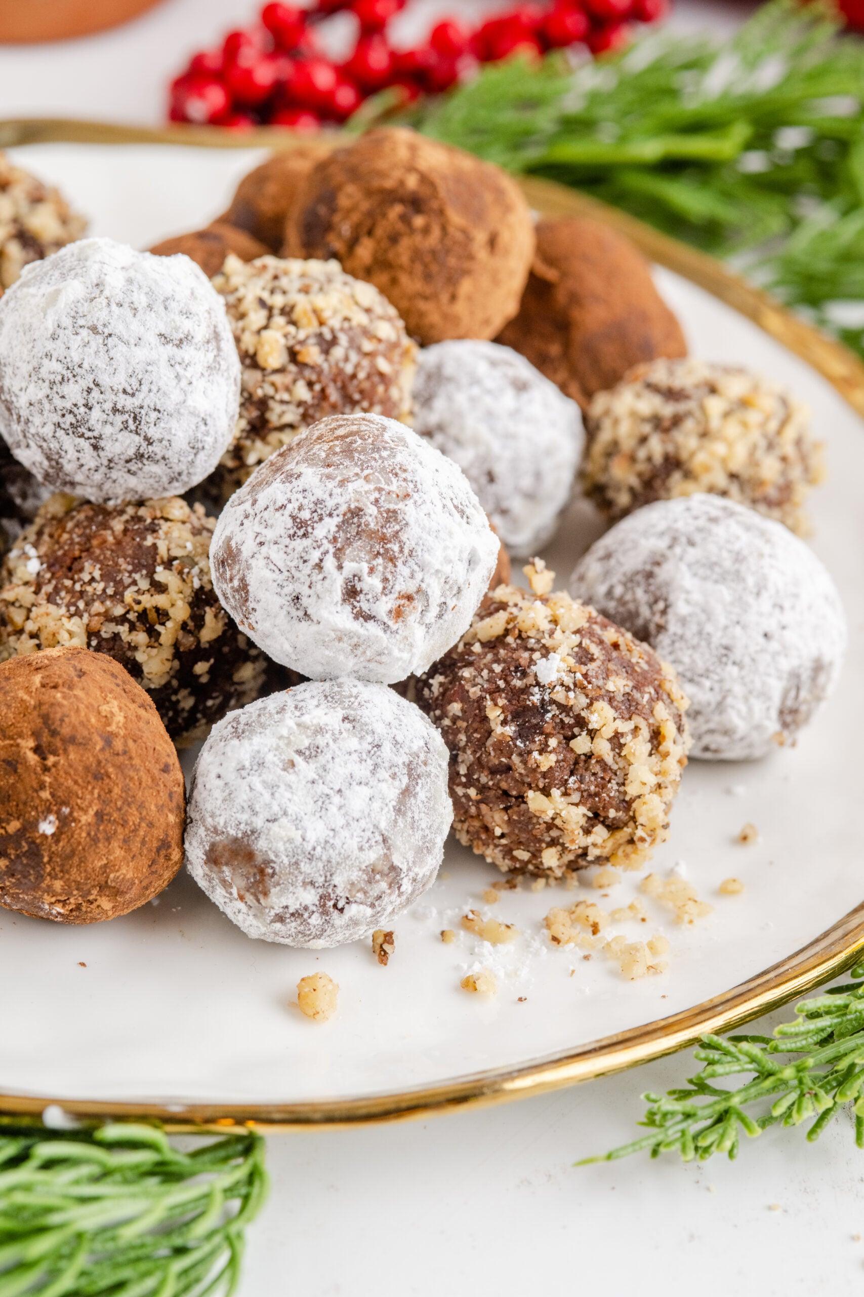 Rum Balls stacked on a white and gold plate with greenery in the background.
