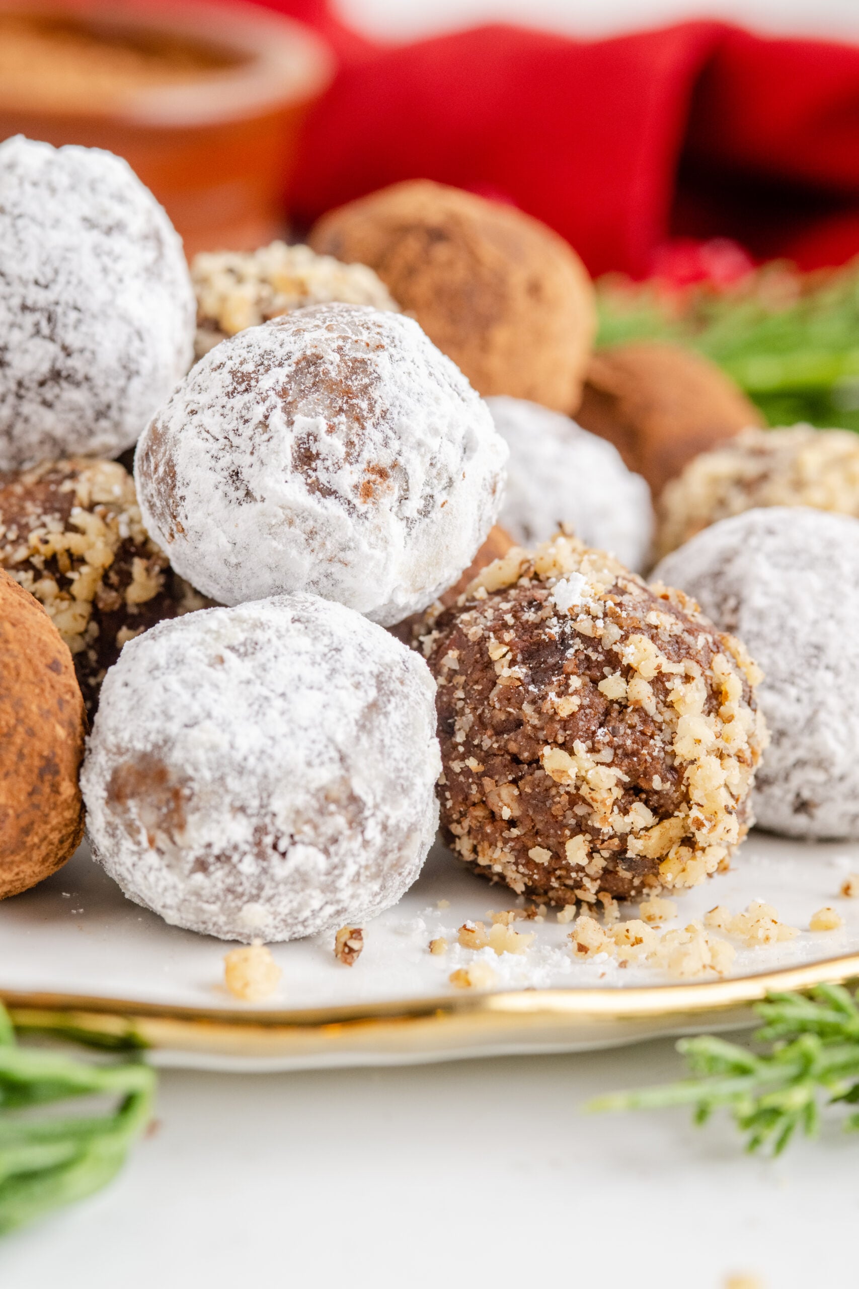 Rum Balls stacked on a white and gold plate with greenery in the background.