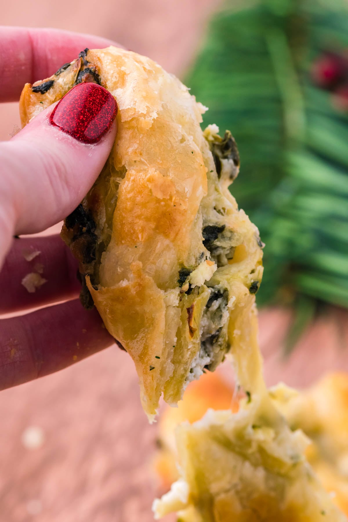 A piece of spinach dip pull apart bread being held up showing the flakey outside layer.