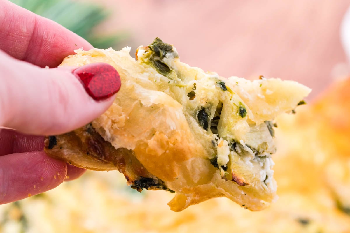 A piece of spinach dip pull apart bread being held up showing the flakey outside layer and spinach dip filling.