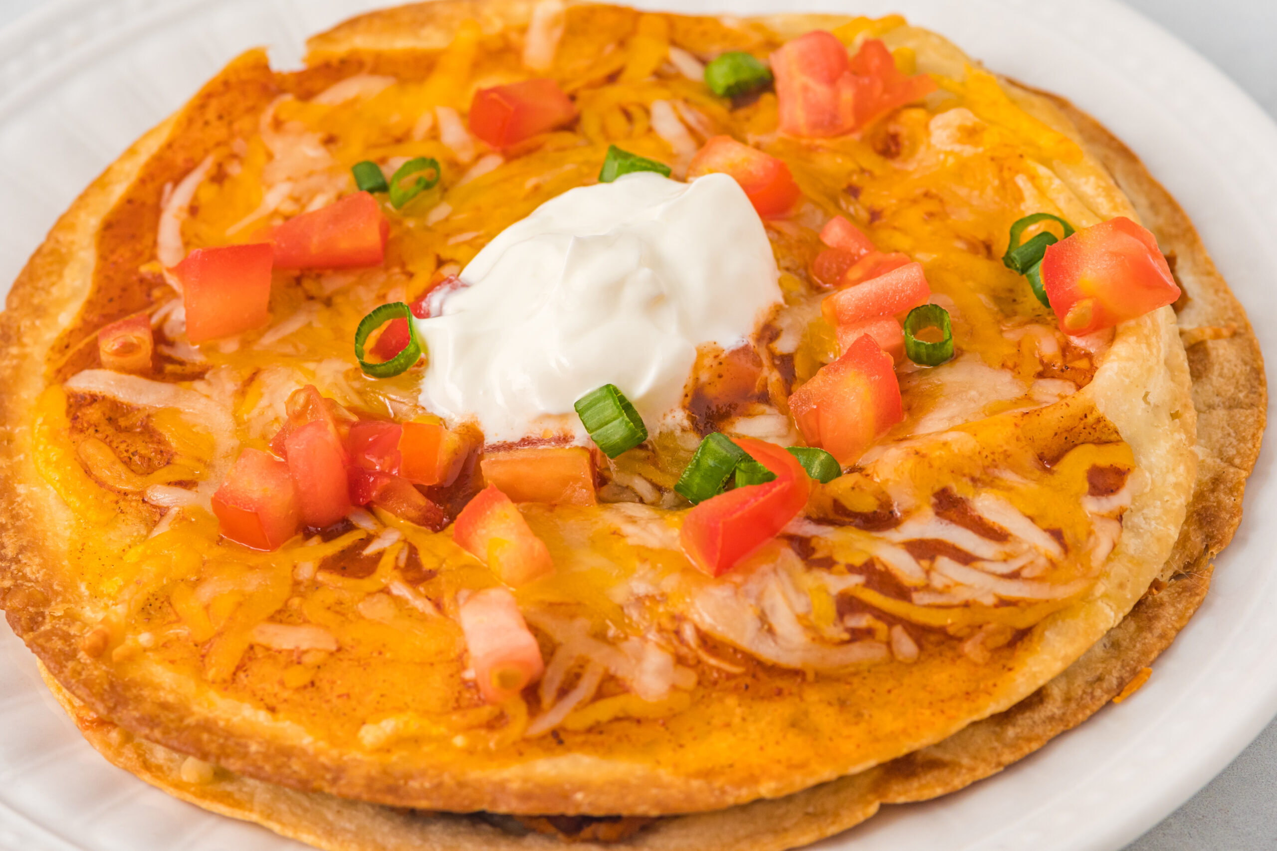 Up close photo of a mexican pizza topped with sour cream, tomatoes and green onions
