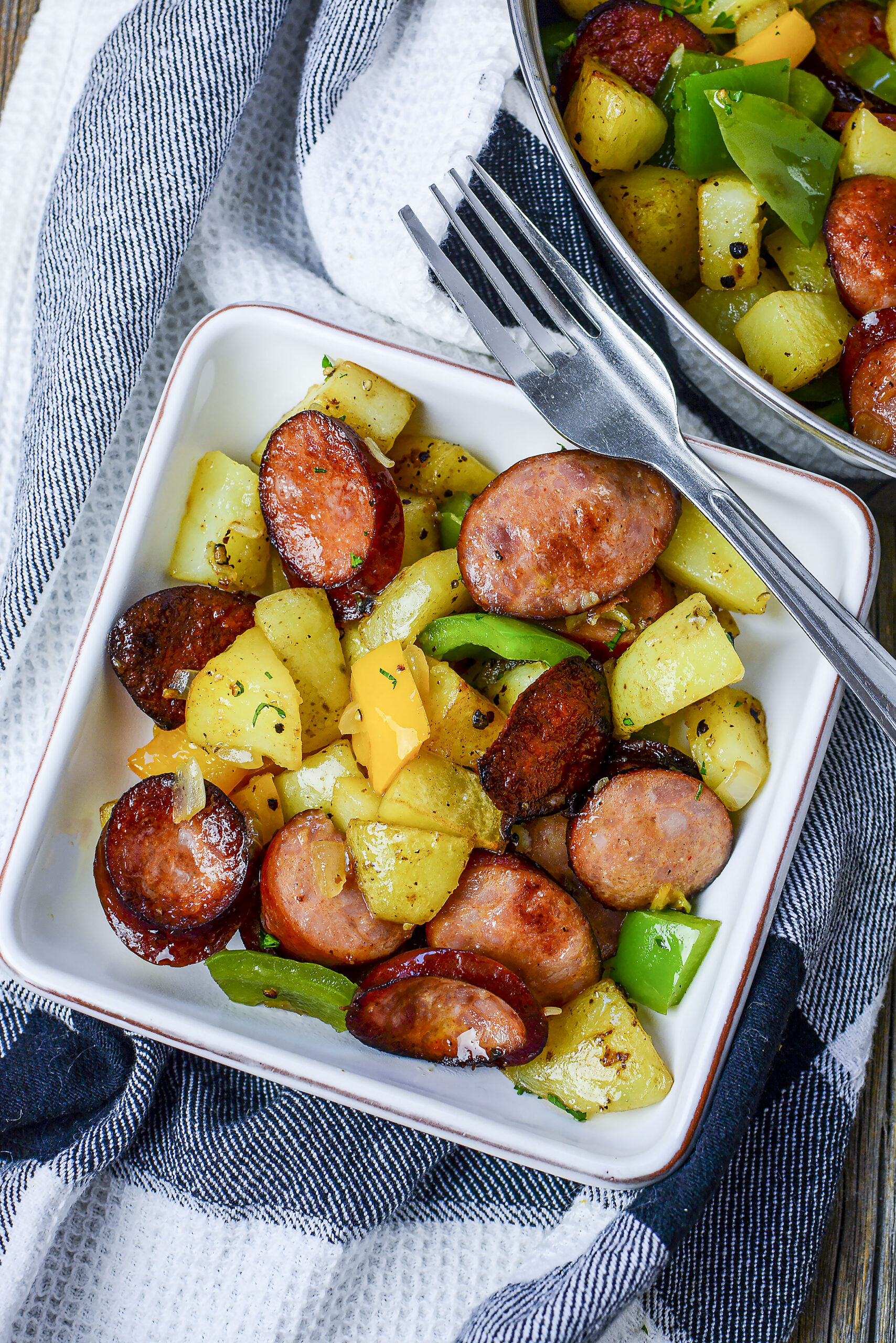 Sausage peppers and potatoes plated on a white plate with a silver fork.