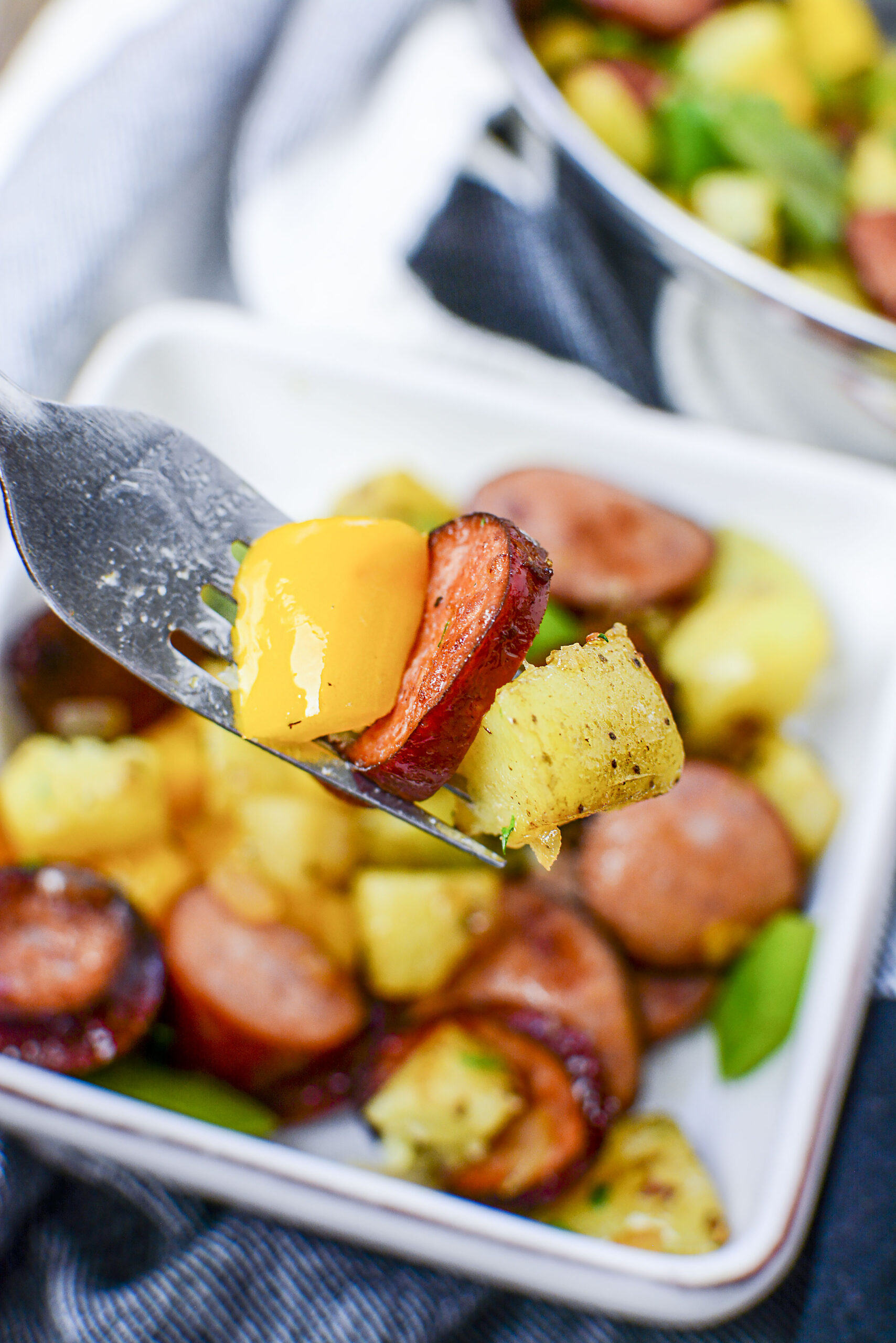 close up of sausage peppers and potatoes on a silver fork.