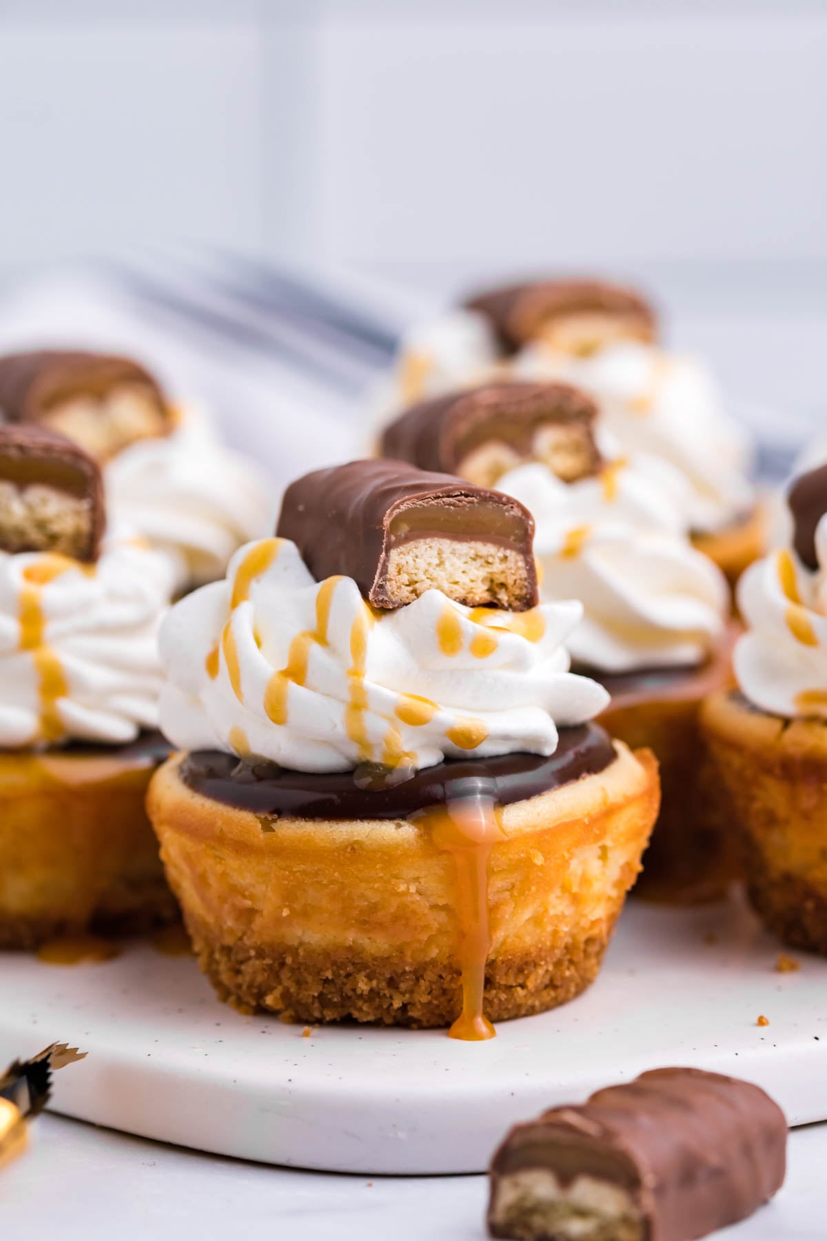 Side view of a Mini Twix Cheesecake topped with whipped cream, caramel drizzle, and Twix candy.