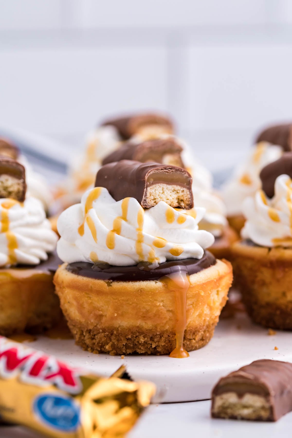 Side view of a Mini Twix Cheesecake topped with whipped cream, caramel drizzle, and Twix candy.