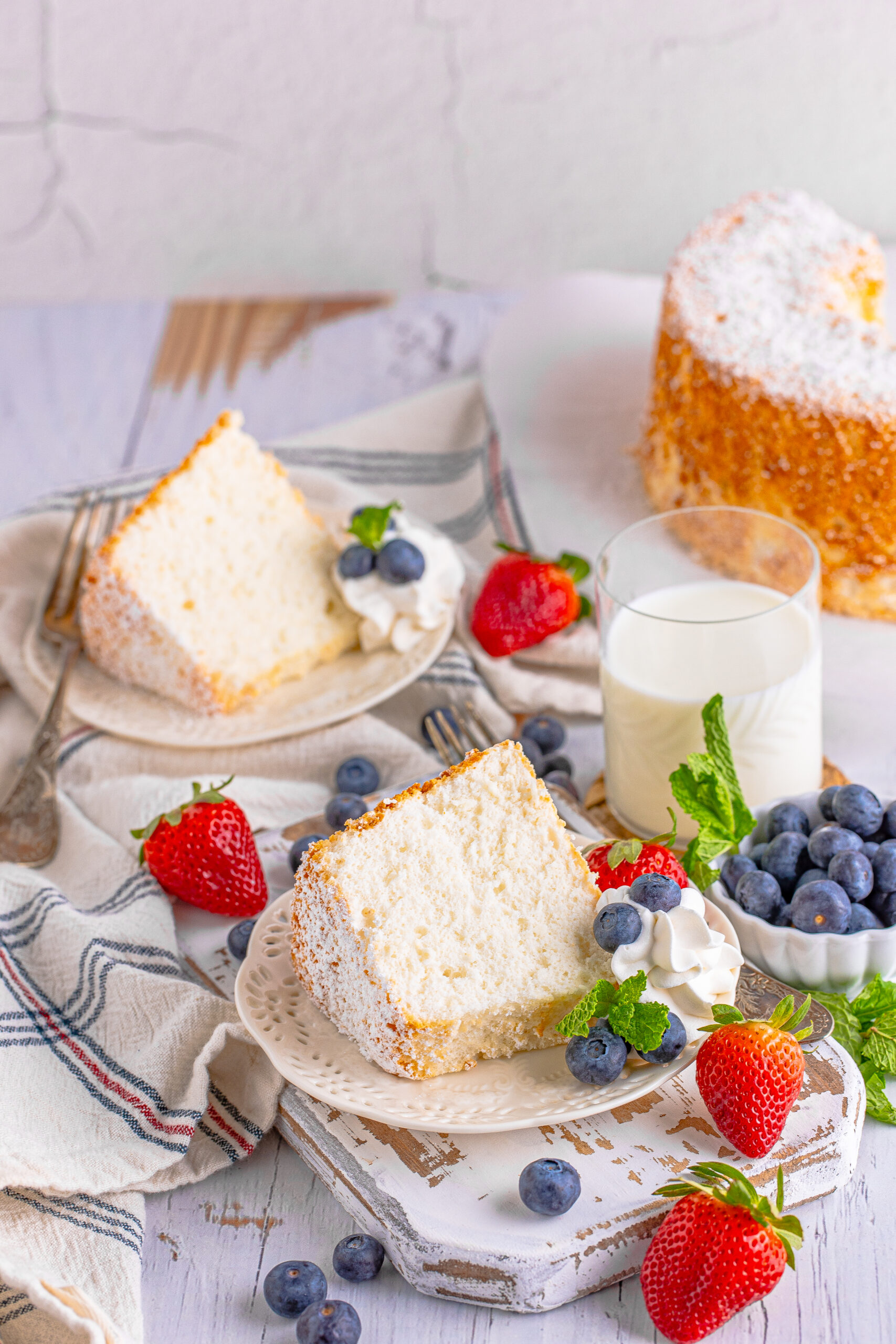 Two pieces of Angel Food Cake on a white plate with whipped cream, fresh berries, and mint