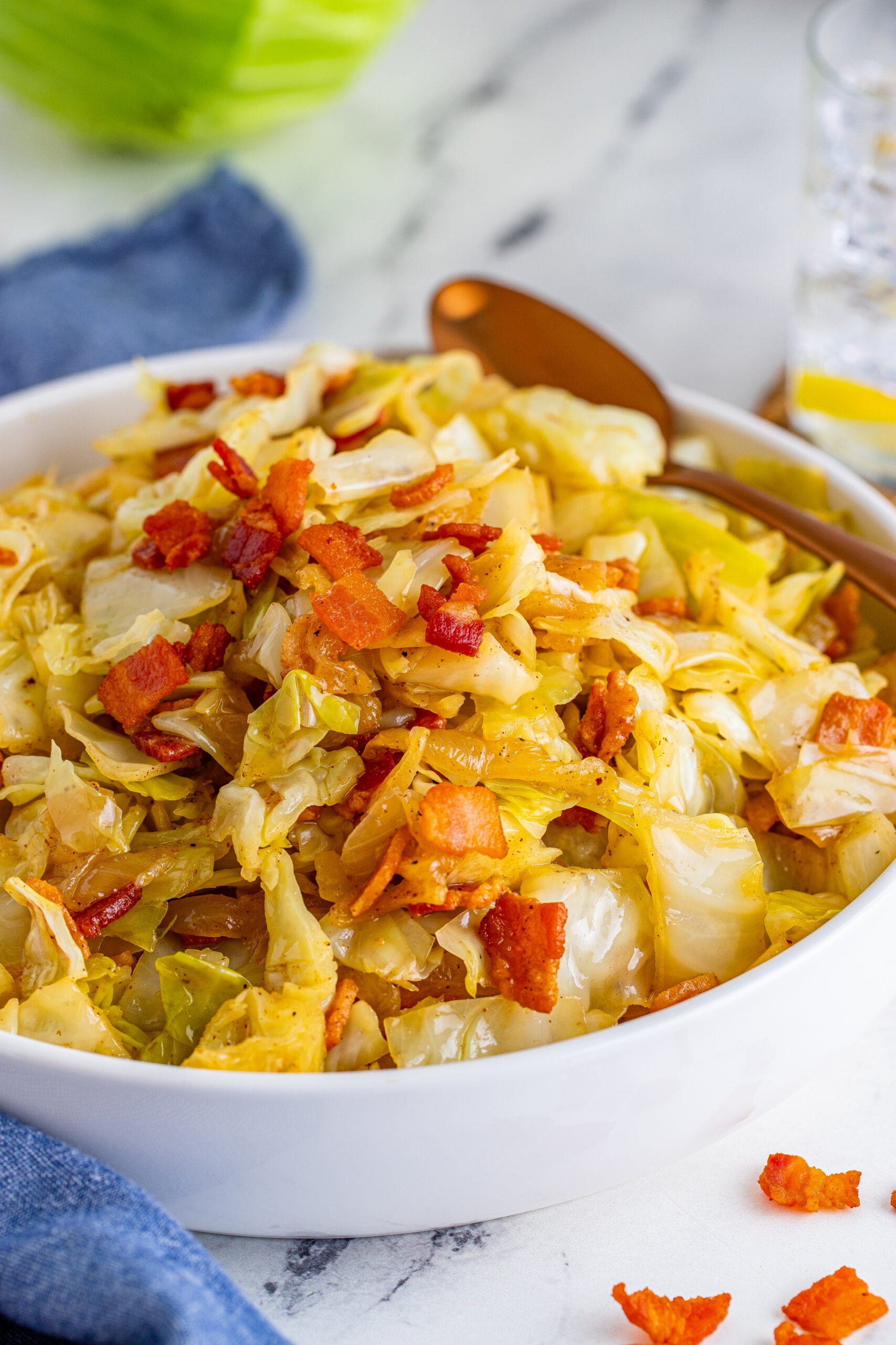 Bacon Fried Cabbage in a white bowl topped with bacon with a gold spoon on the side