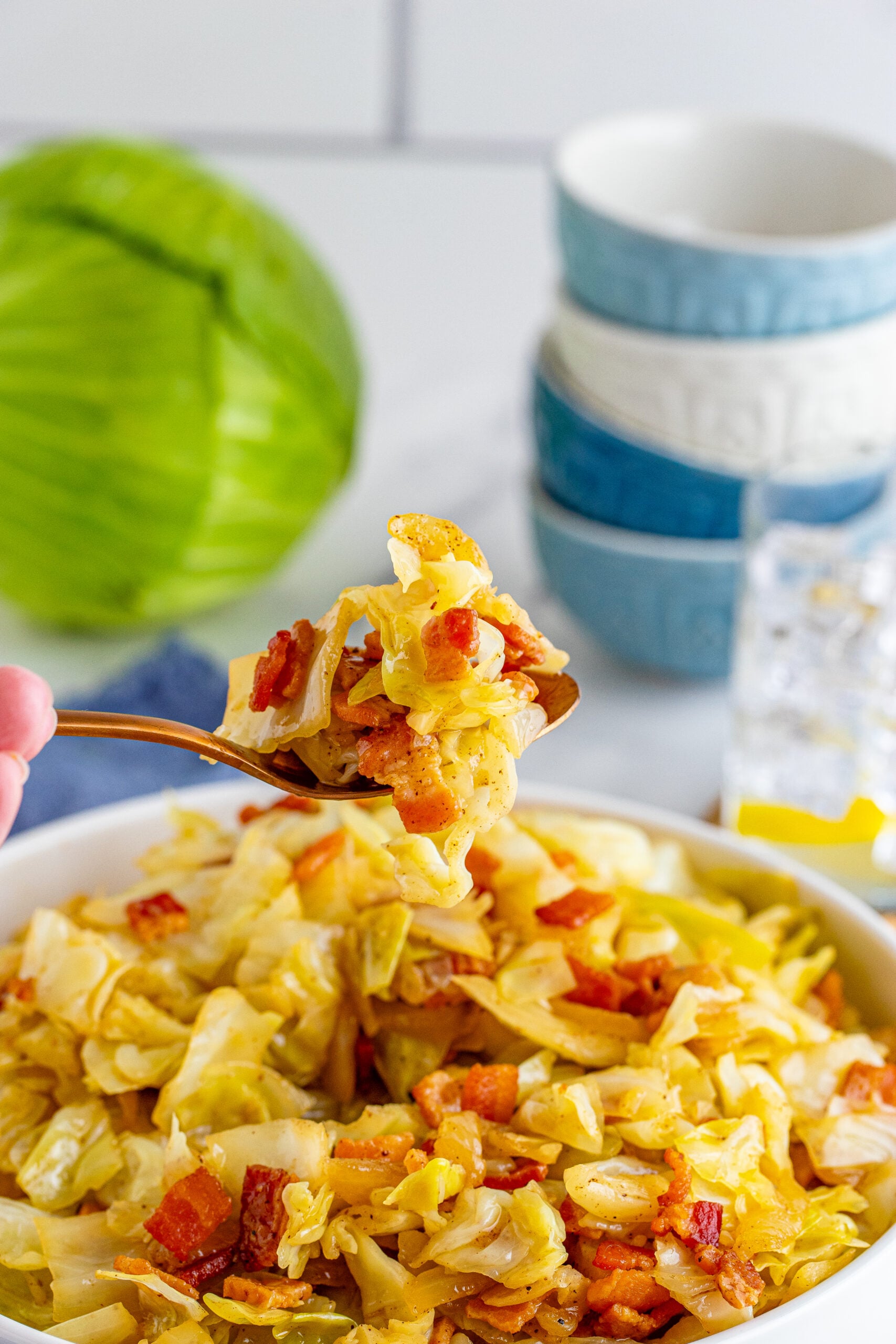 Fried Cabbage in a white bowl with a bite being removed with a gold spoon. 